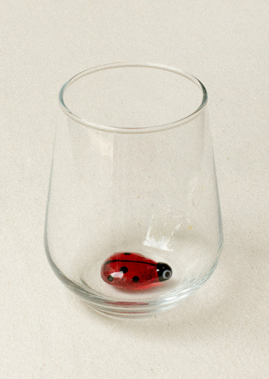 A clear tumbler glass with lampwork ladybug detail at inner bottom.