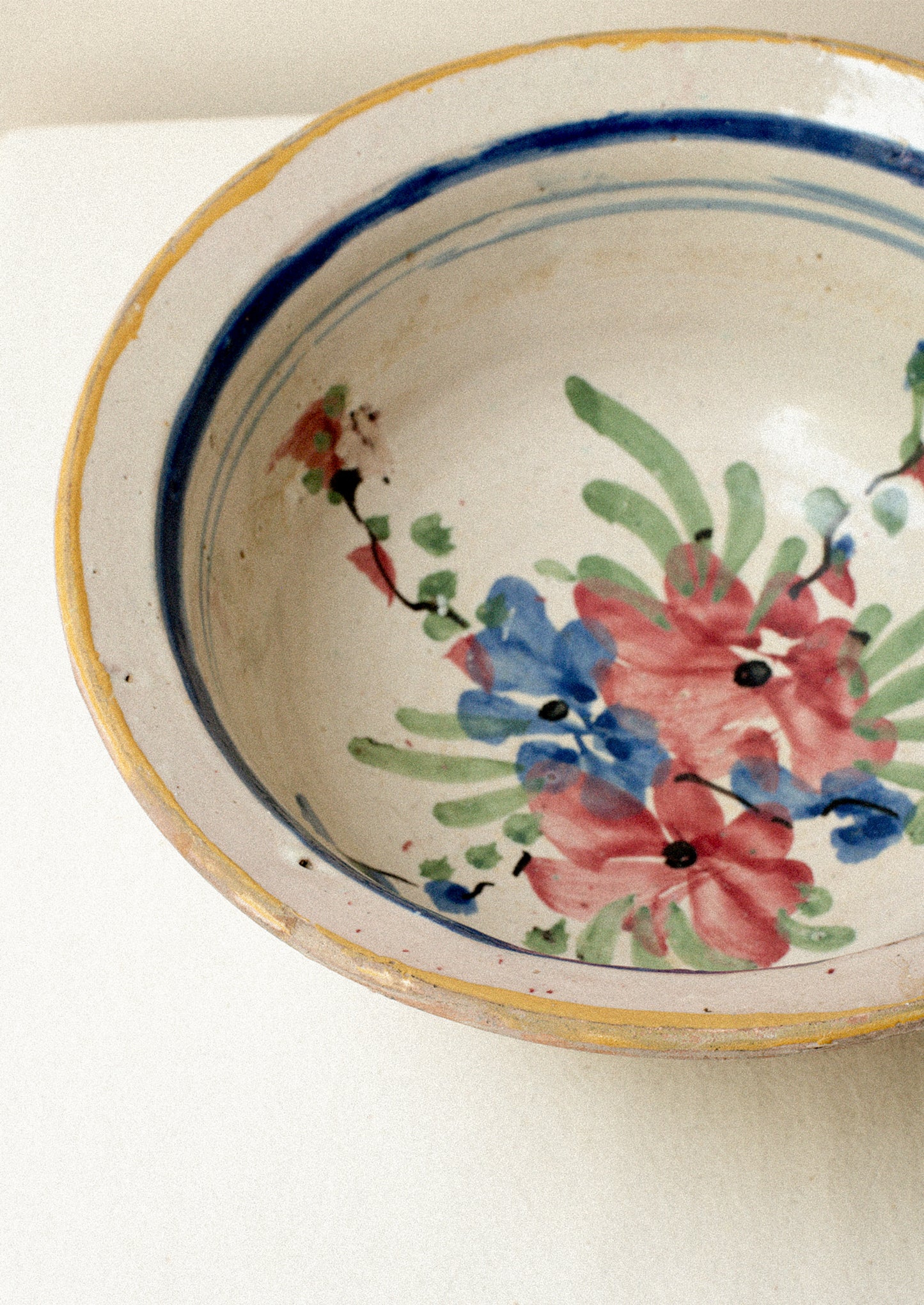 An antique ceramic serving bowl with painted blue rim and pink floral pattern.