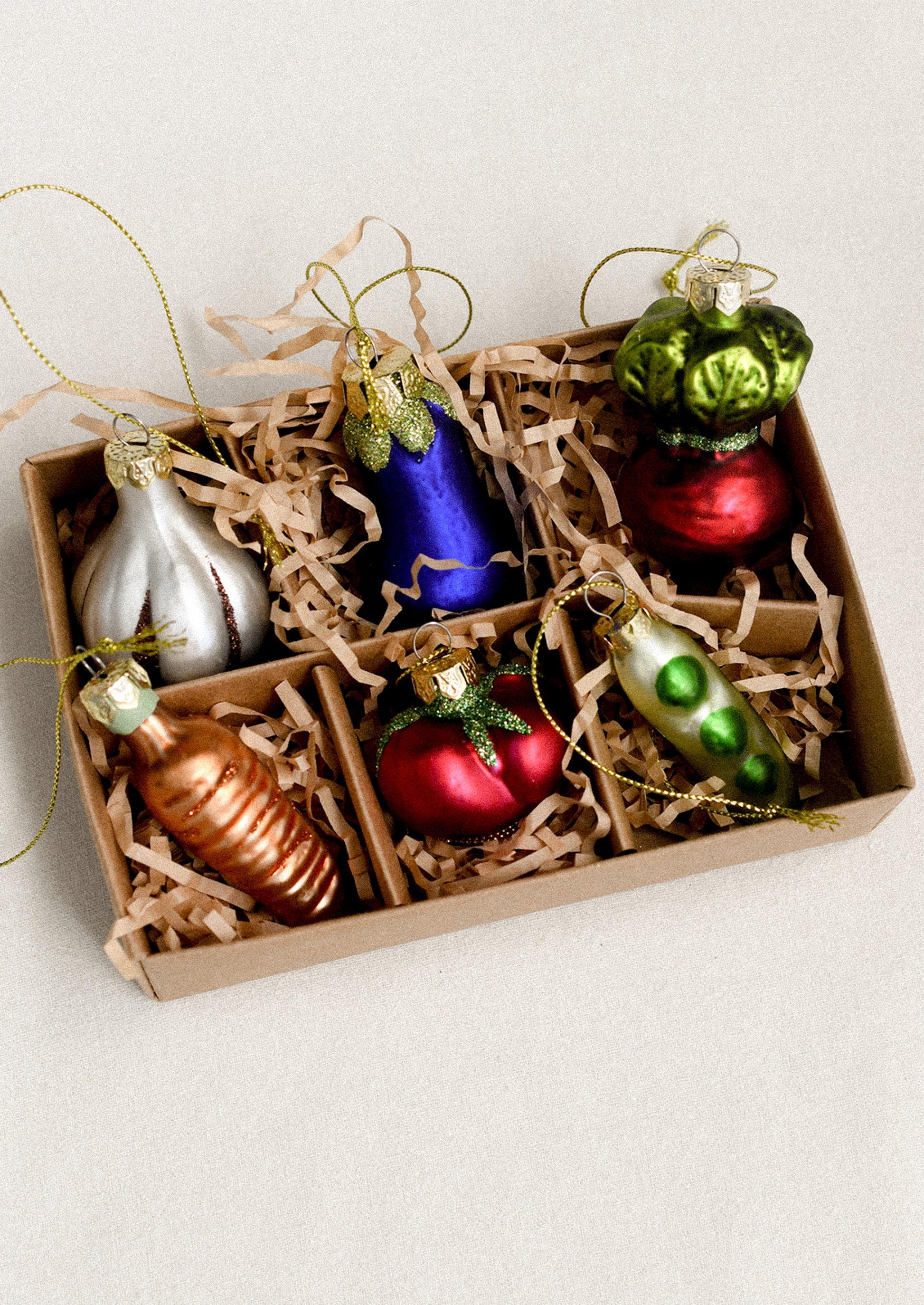 Set of colorful glass vegetable-shaped ornaments in a gift box with crinkle paper.