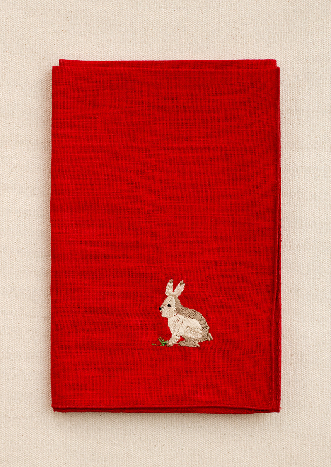 A red linen napkin with embroidered bunny motif.
