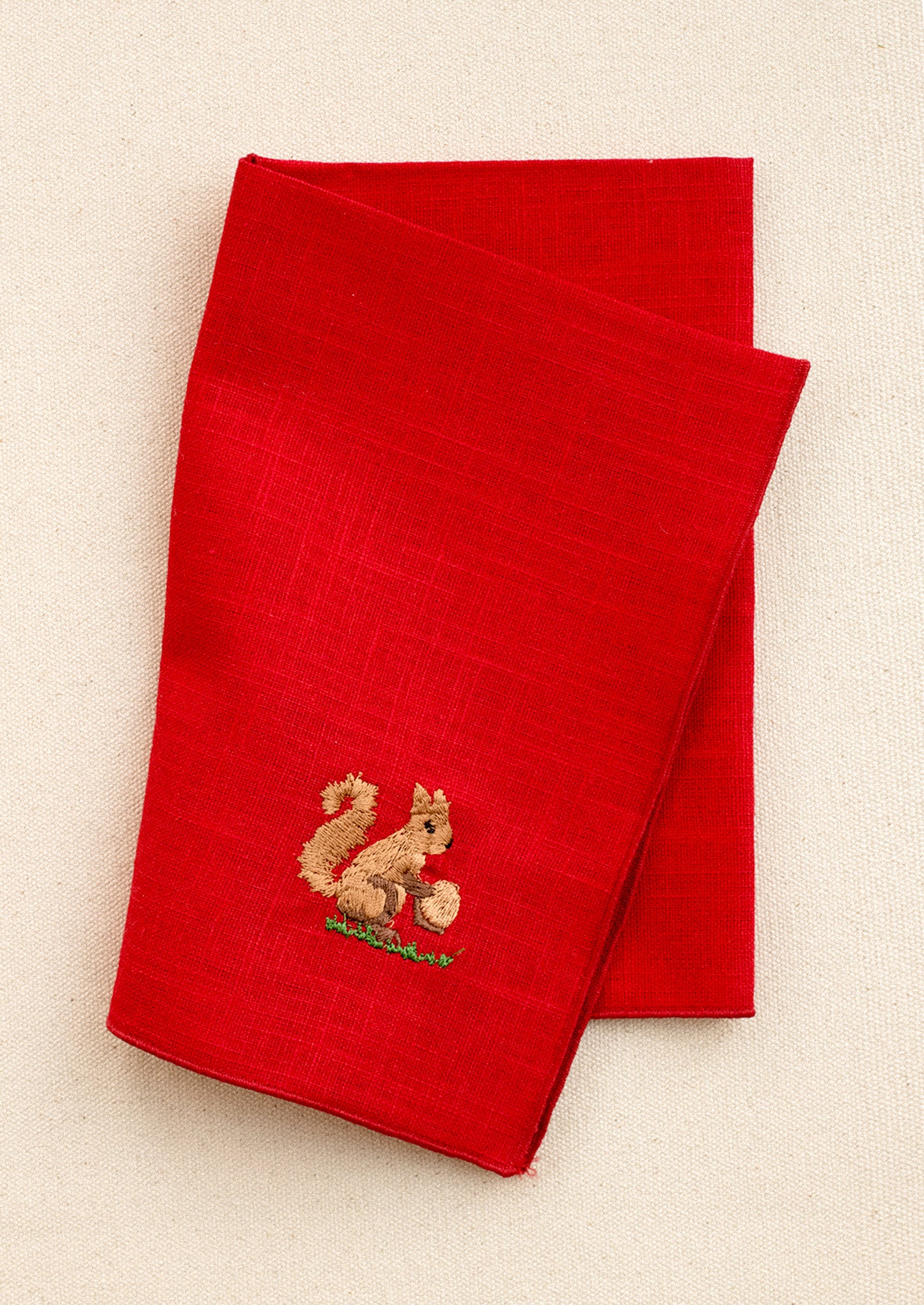 A red linen napkin with embroidered squirrel motif.