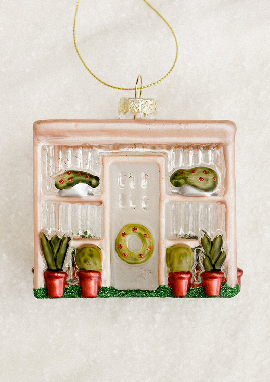A decorative glass ornament depicting a greenhouse, with wreath decorations.