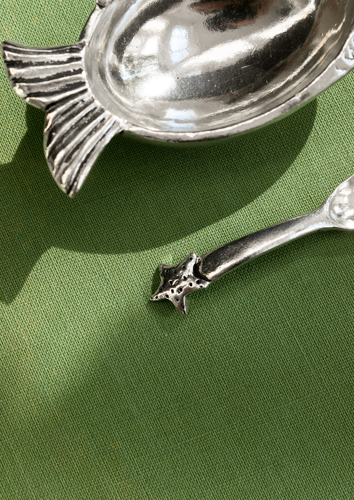 Silver fish-shaped spoon rest and decorative spoon on a green surface