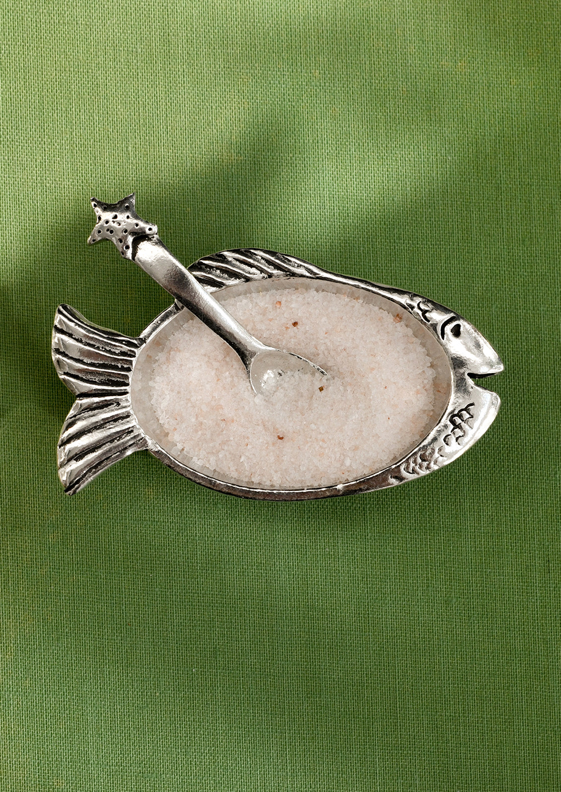 Decorative fish-shaped salt cellar with a spoon on a green background
