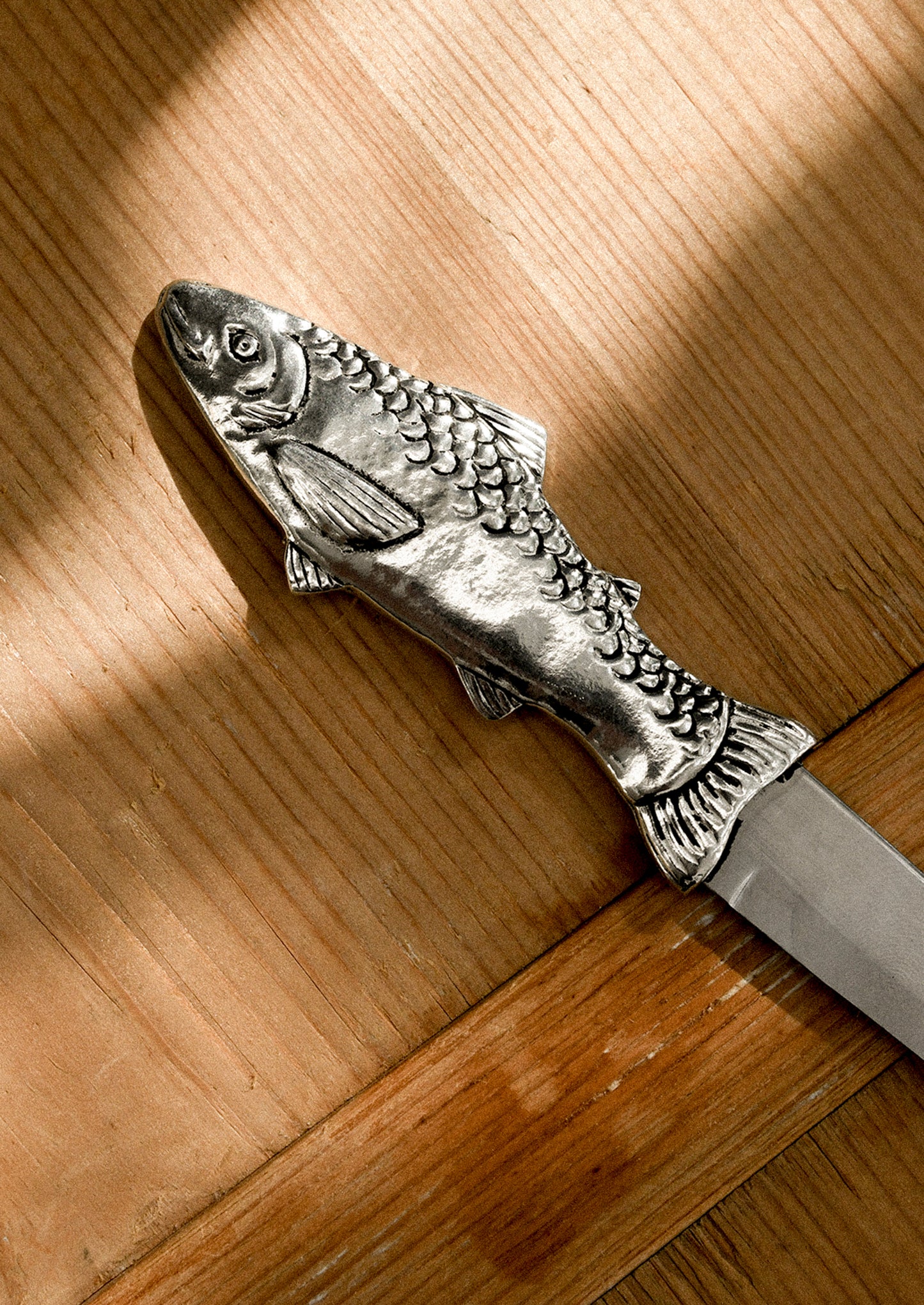 A pewter serrated cheese knife with pronged end, and fish-shaped handle.