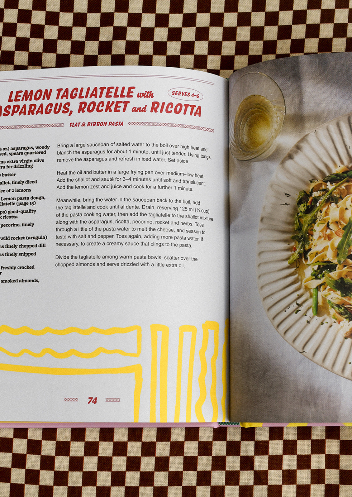 Open cookbook showing a recipe for lemon tagliatelle with asparagus, rocket, and ricotta on a checkered tablecloth.