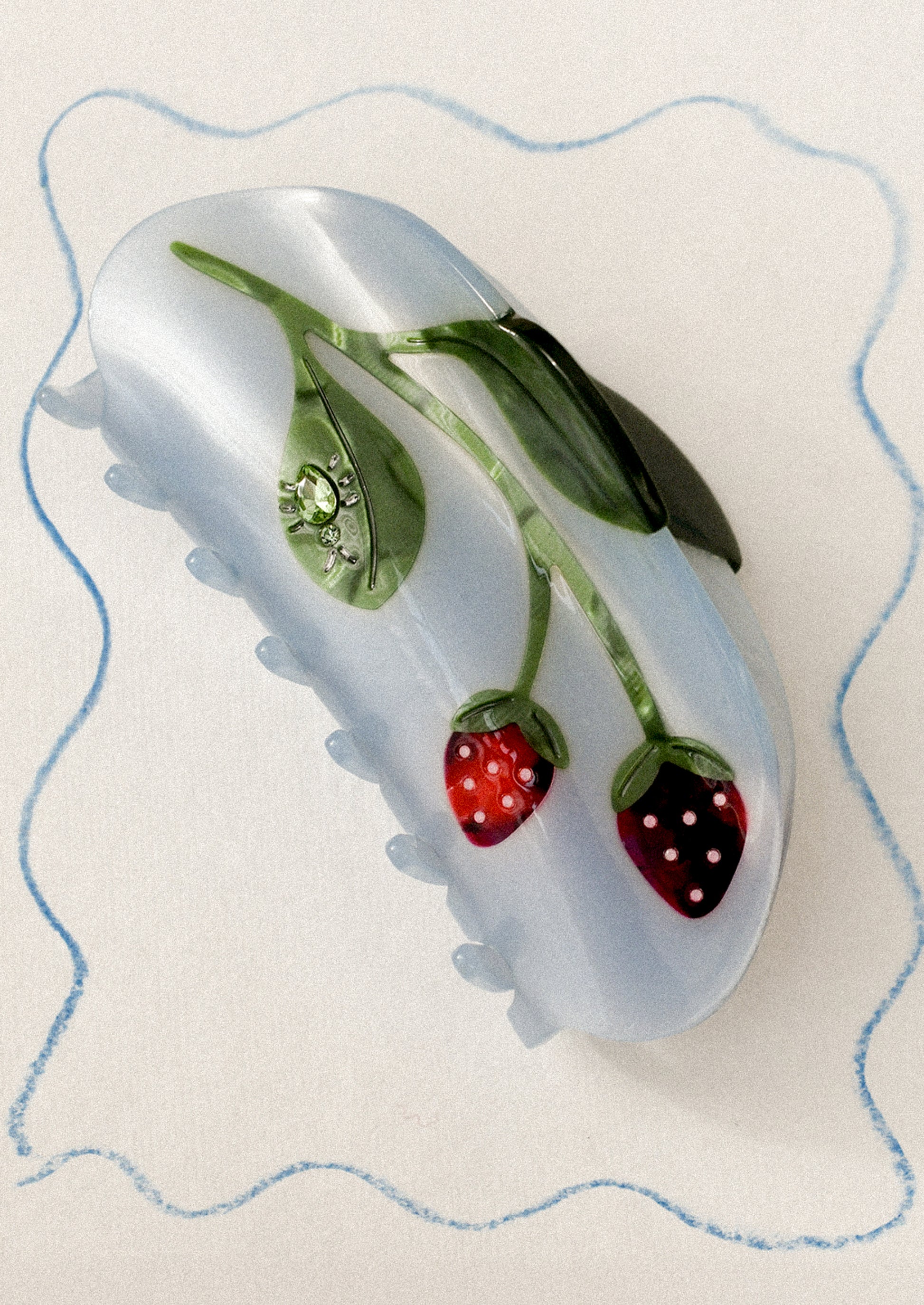 A blue hair claw with strawberry motif and jeweled bug on leaf.