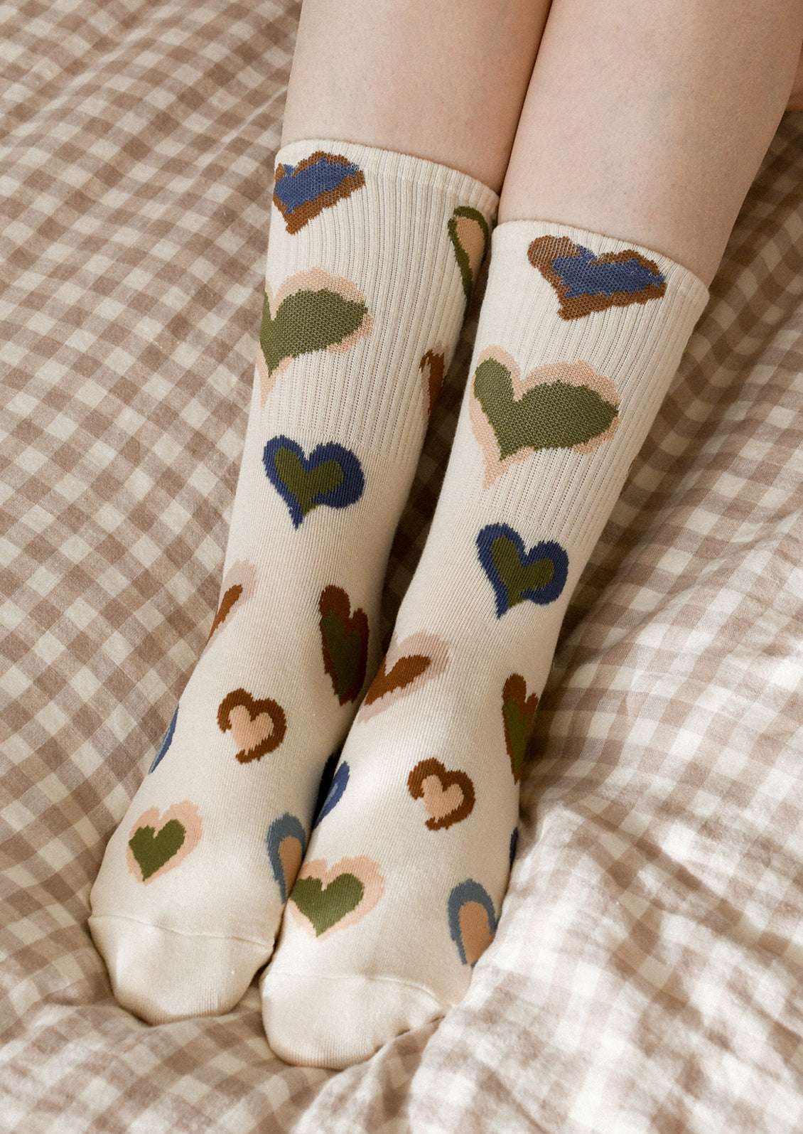 A person wearing heart patterned socks in cream with green, blue and brown pattern.