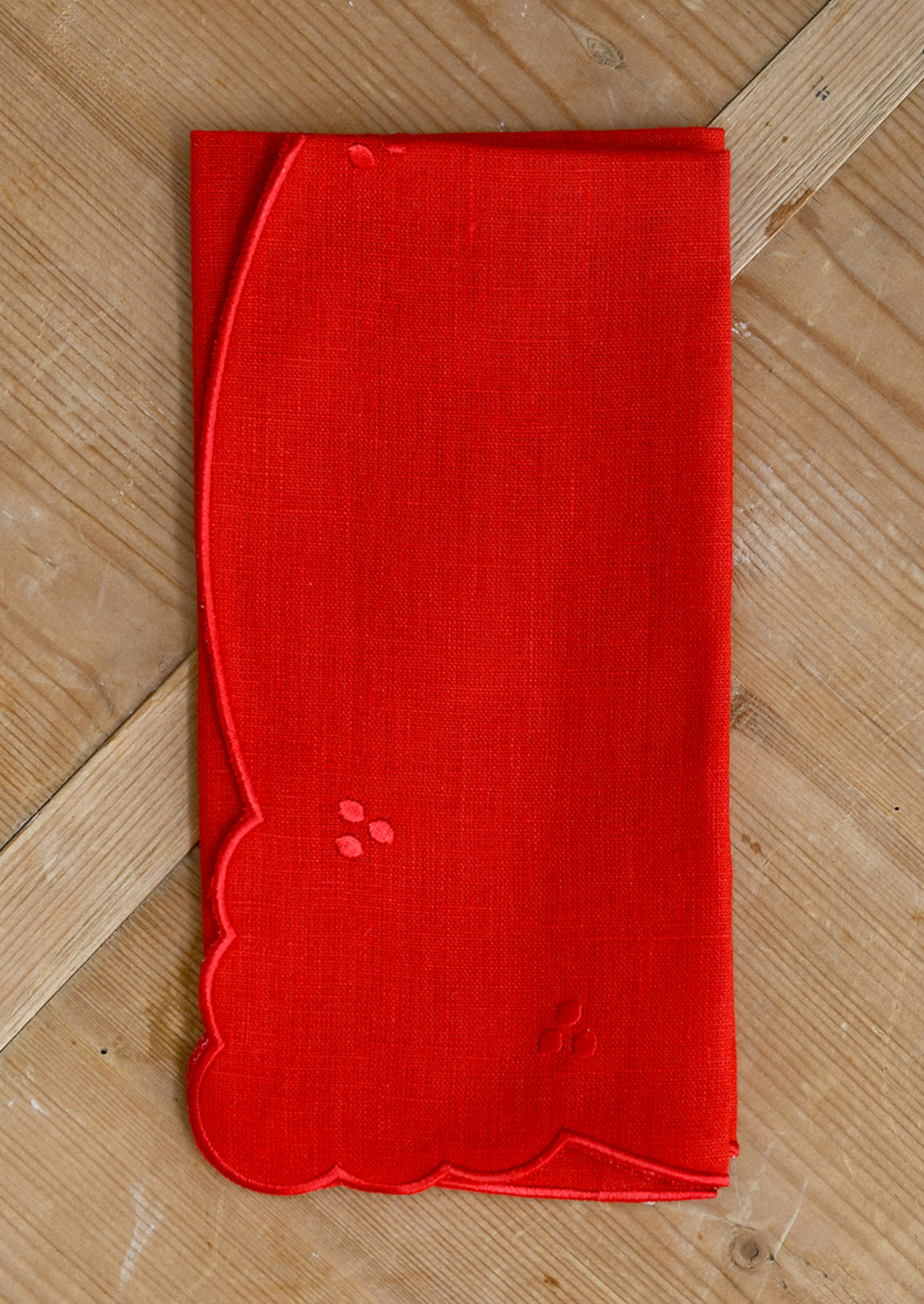 A bright red linen napkin with scalloped embroidery details.