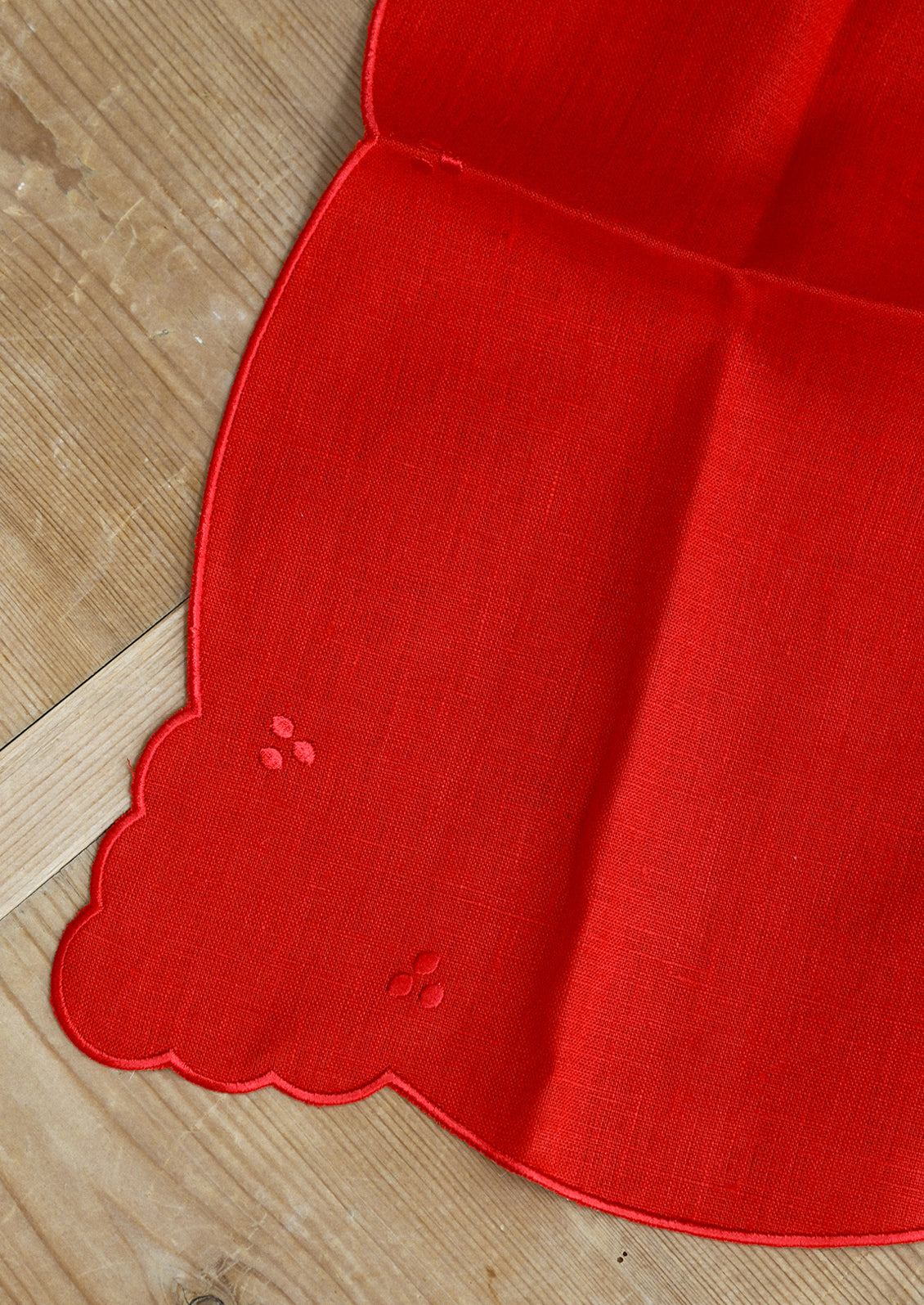 A bright red linen napkin with scalloped embroidery details.