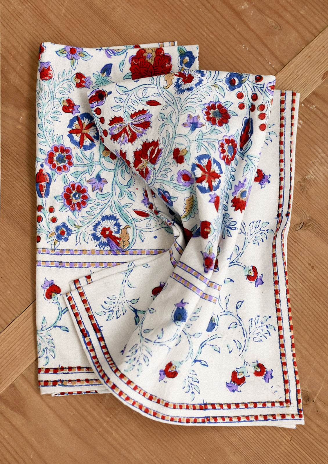 Set of floral-patterned napkins in white with red, lavender and aqua color scheme on a wooden surface.