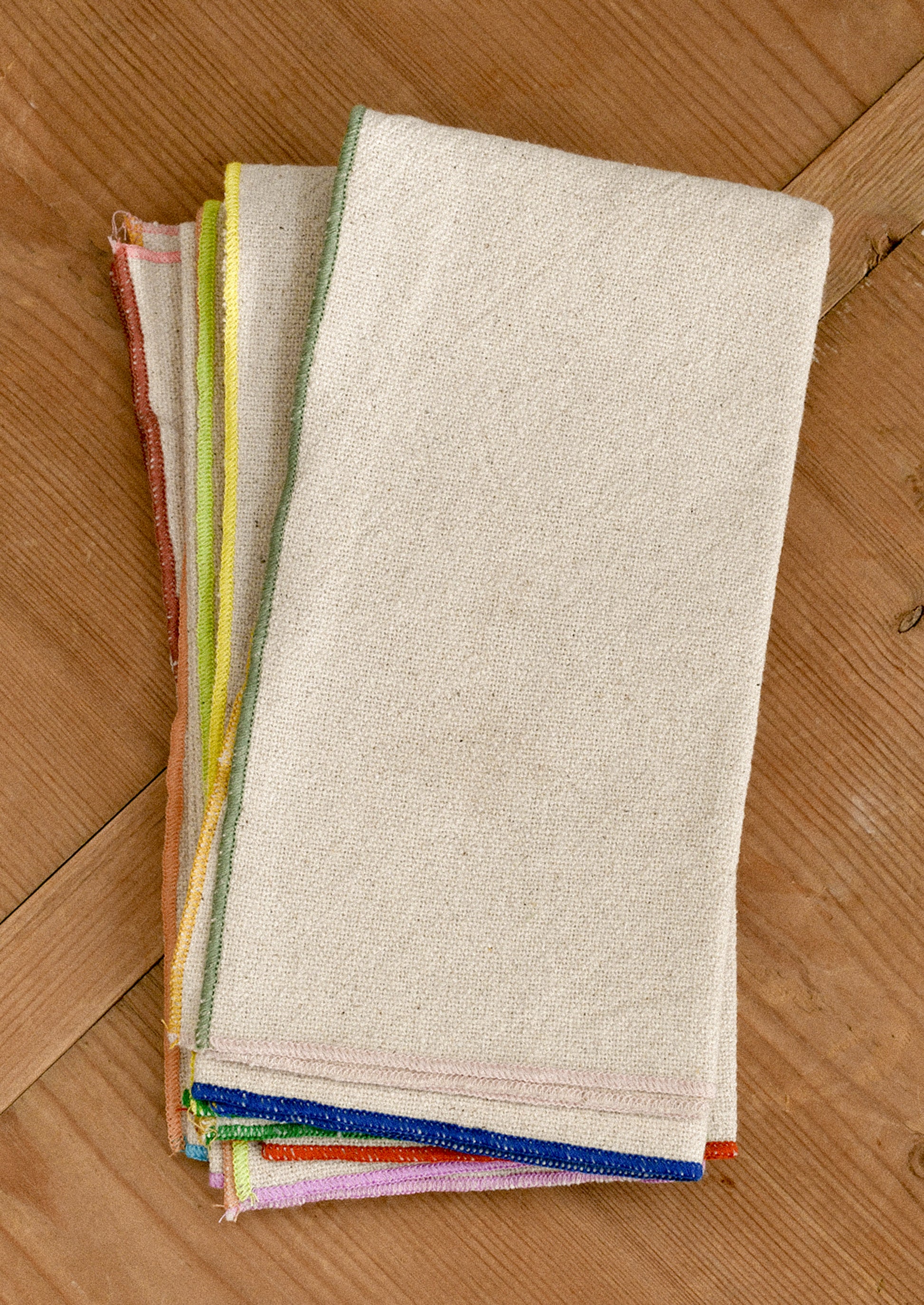 Folded cotton napkins with colorful edges on a wooden surface