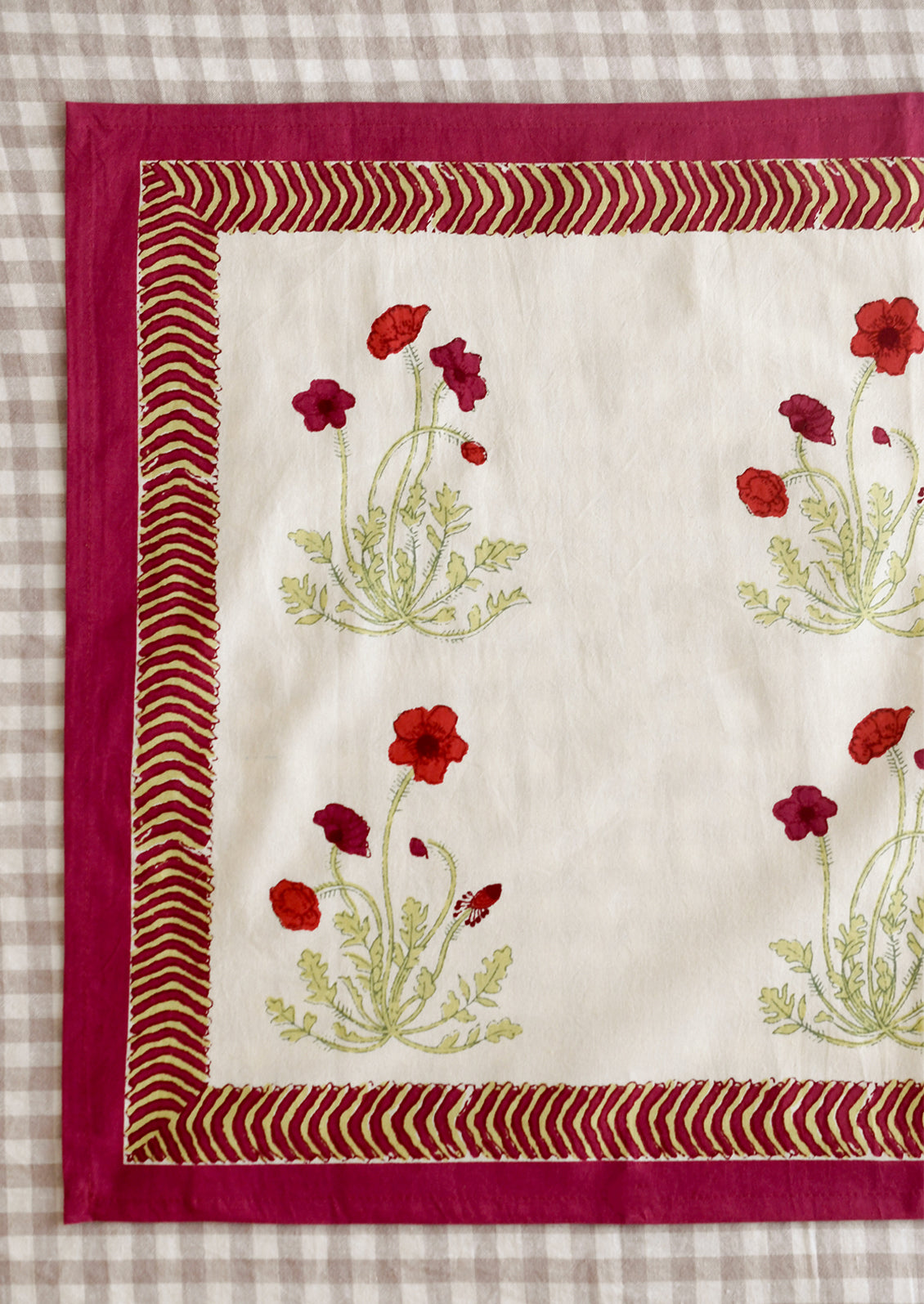 A pair of napkins with red poppy print and geometric red and green border.