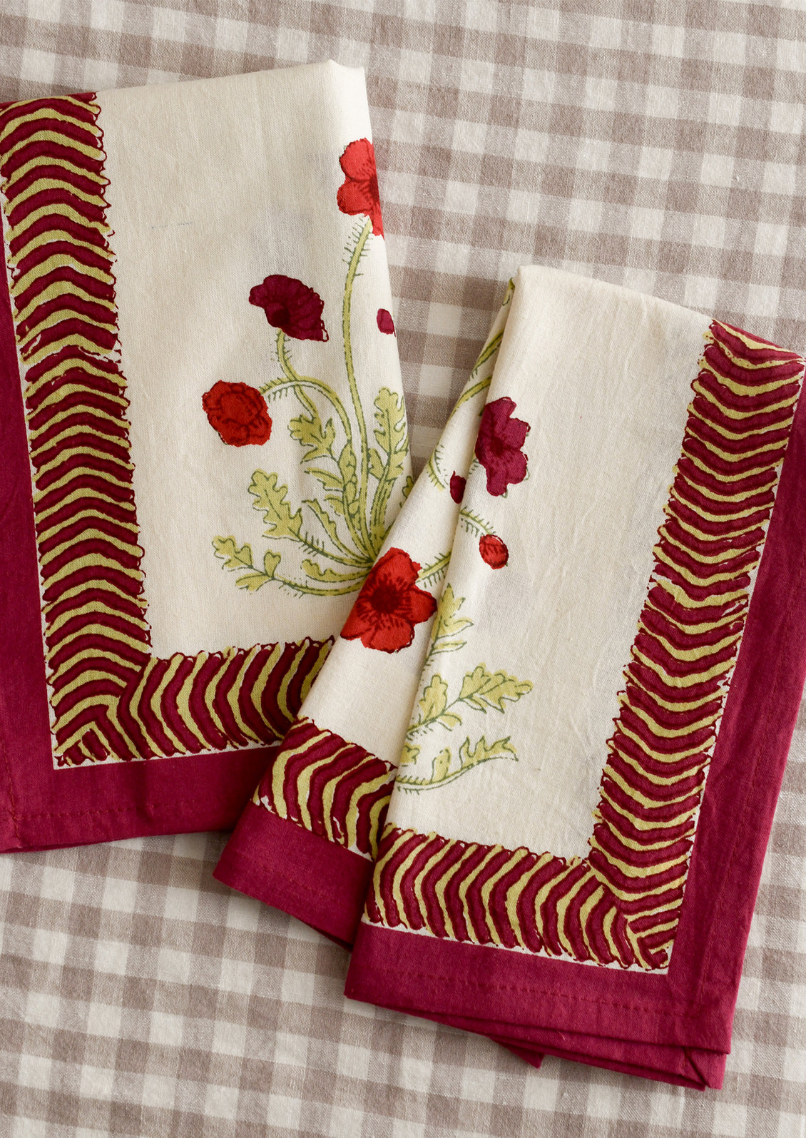 A pair of napkins with red poppy print and geometric red and green border.