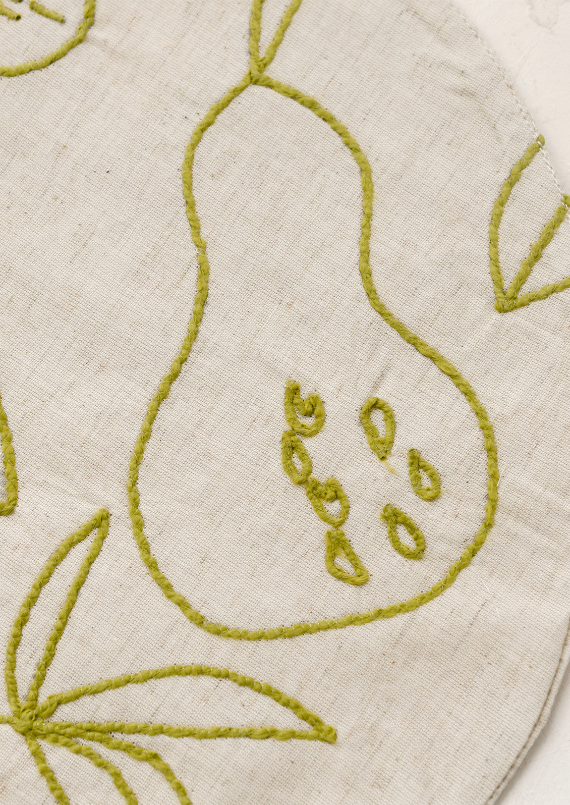 Round placemat with embroidered fruit design in green.