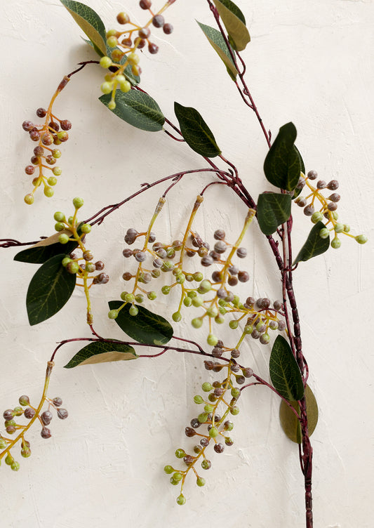 Artificial berry branch with green leaves and small berries on a white background