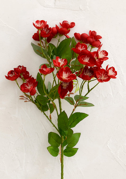 Red artificial flowers with green leaves on a white background
