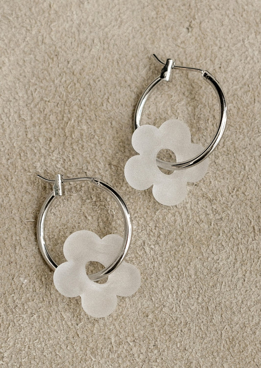 Silver hoop earrings with white flower-shaped charms on a beige background