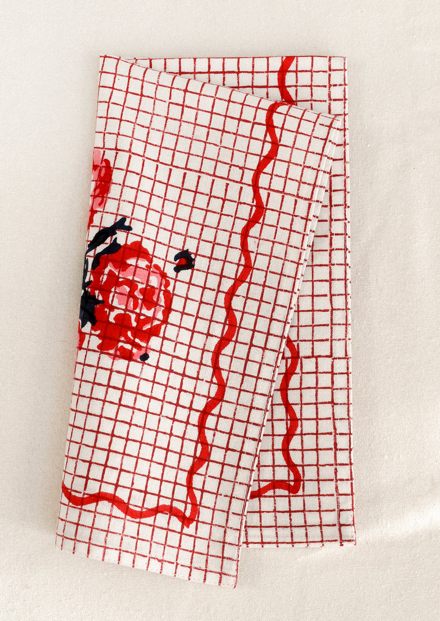 Red grid patterned cloth napkin with floral design and squiggle border.