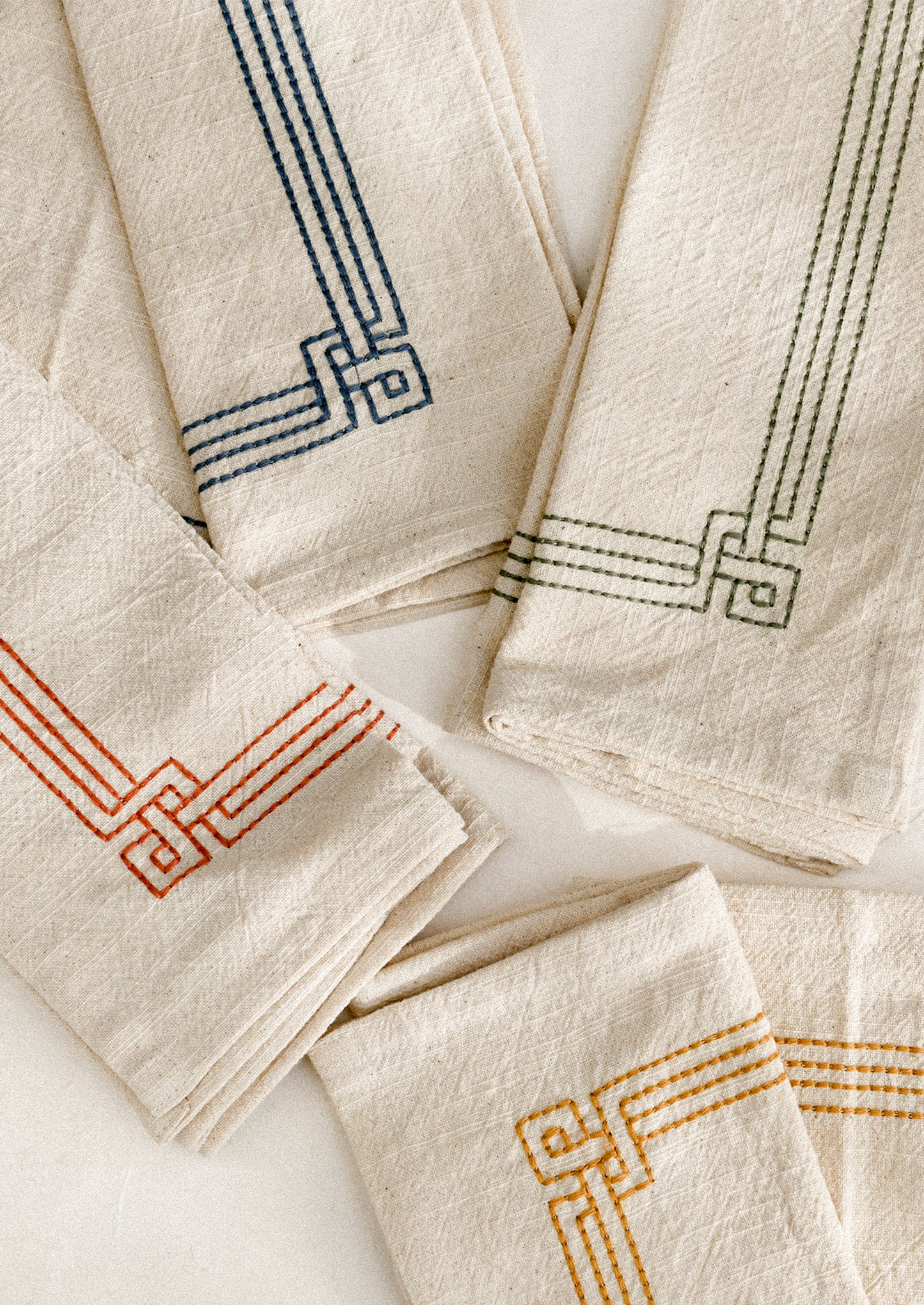 Set of beige napkins with embroidered geometric patterns in various colors on a white surface.