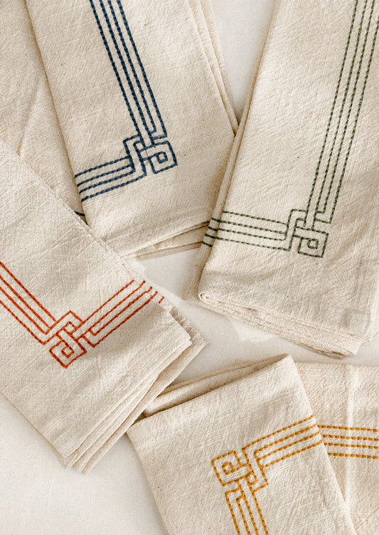 Set of beige napkins with embroidered geometric patterns in various colors on a white surface.