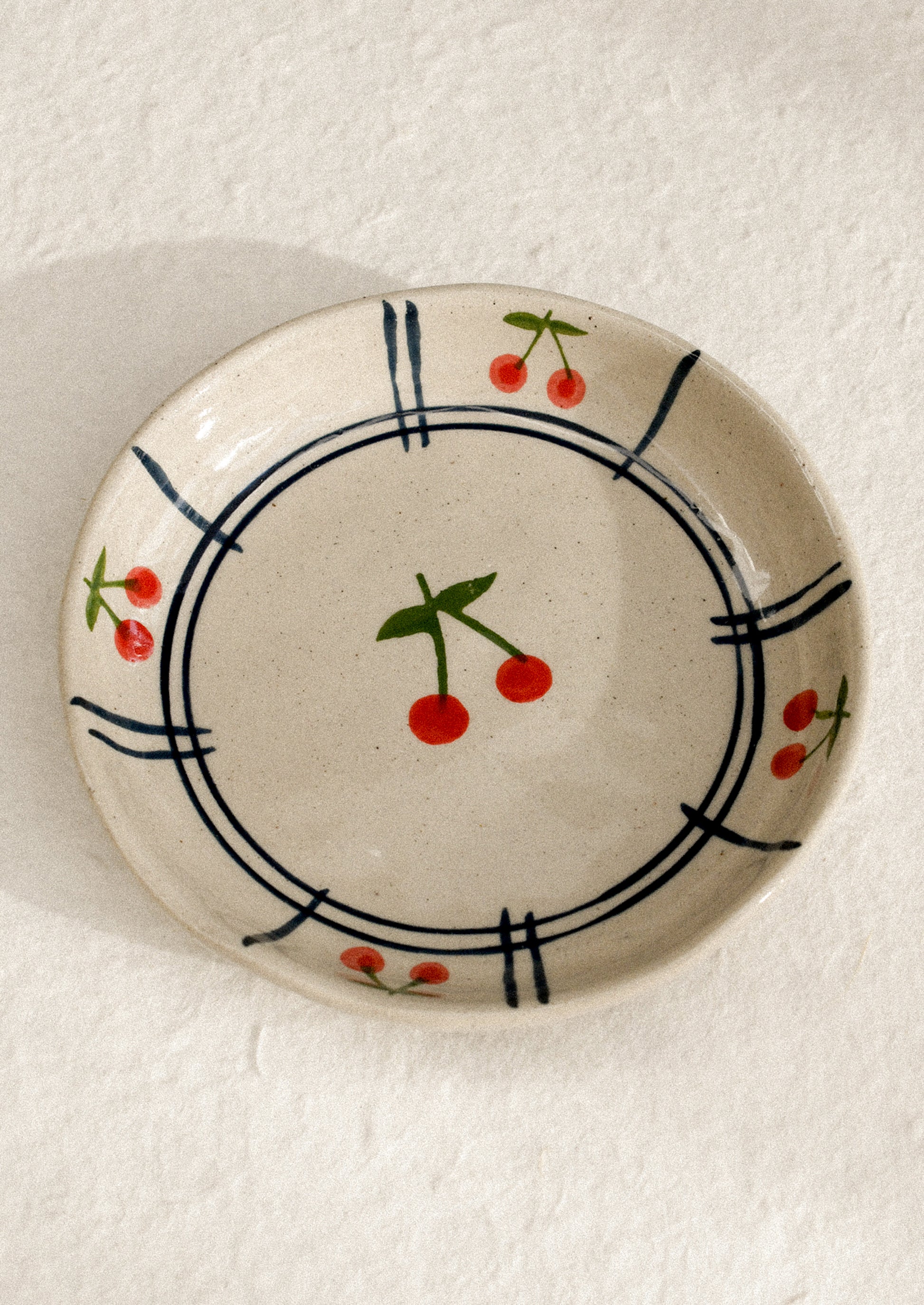 A small ceramic dish with raised sides with hand painted cherry motif.
