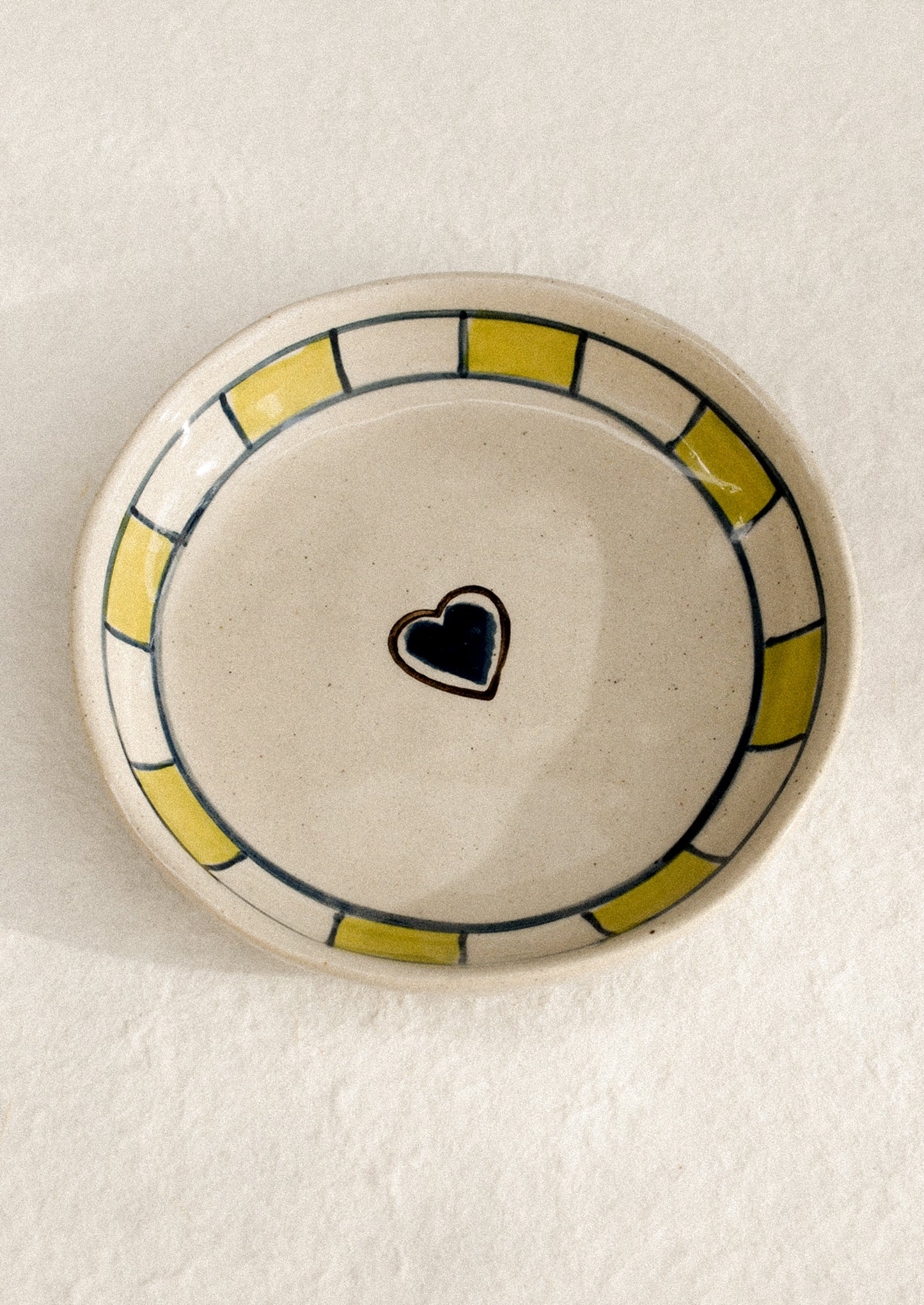 A small ceramic dish with raised sides with hand painted heart motif.