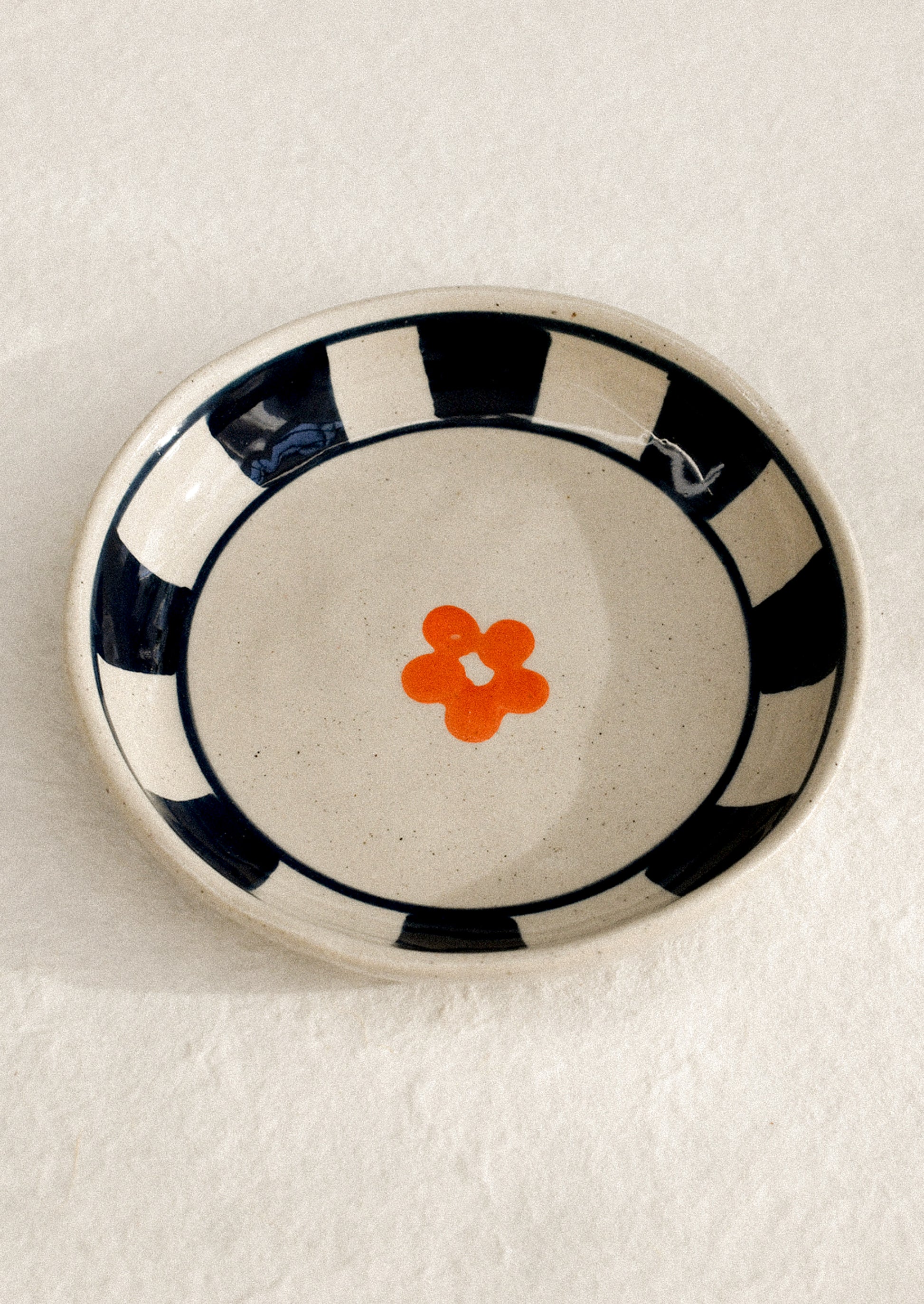 A small ceramic dish with raised sides with hand painted flower motif.