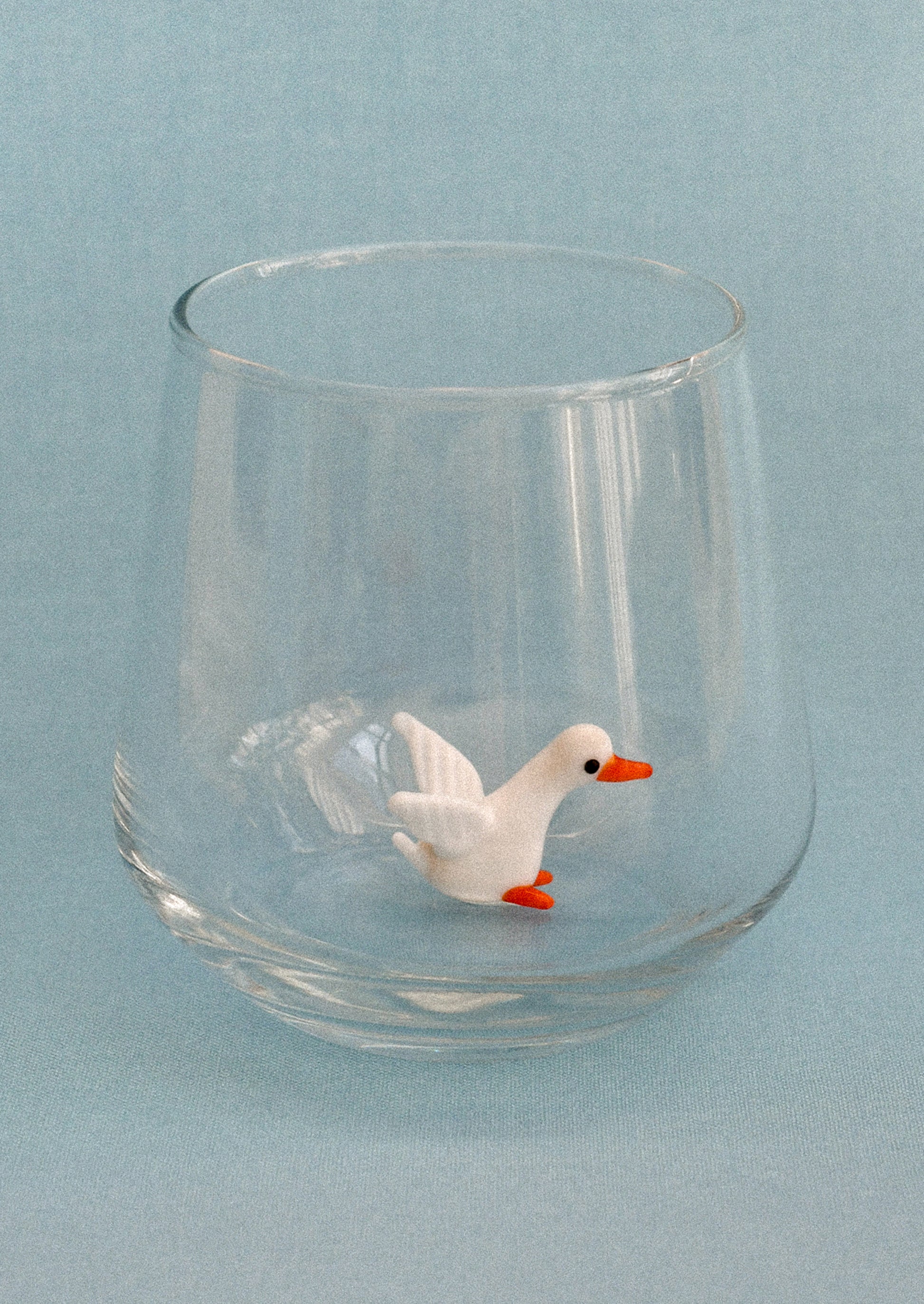 Clear glass tumbler with a small duck figure on a light blue background