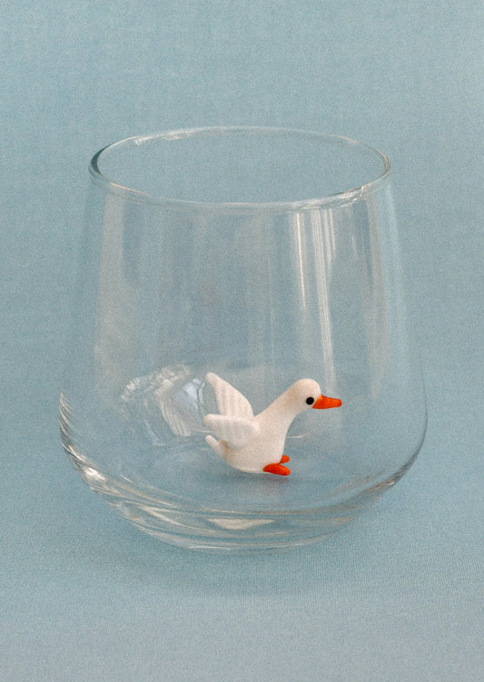 Clear glass tumbler with a small duck figure on a light blue background