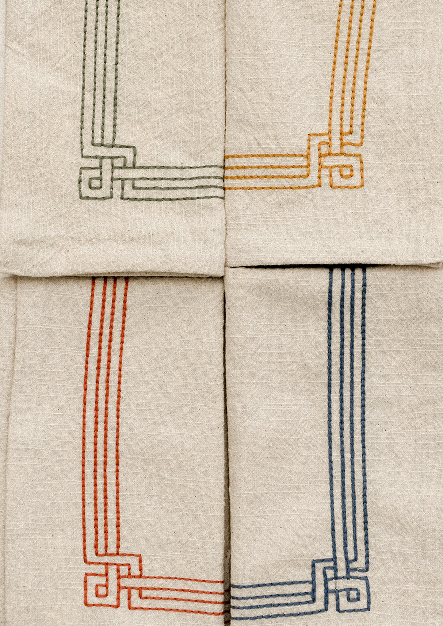 Set of beige napkins with embroidered geometric patterns in various colors on a white surface.