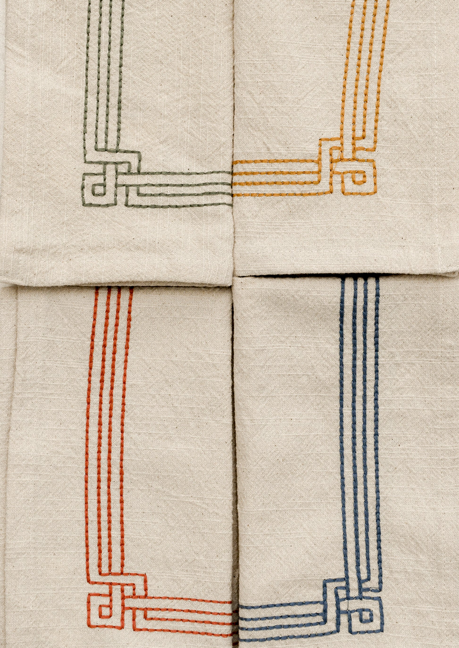 Set of beige napkins with embroidered geometric patterns in various colors on a white surface.