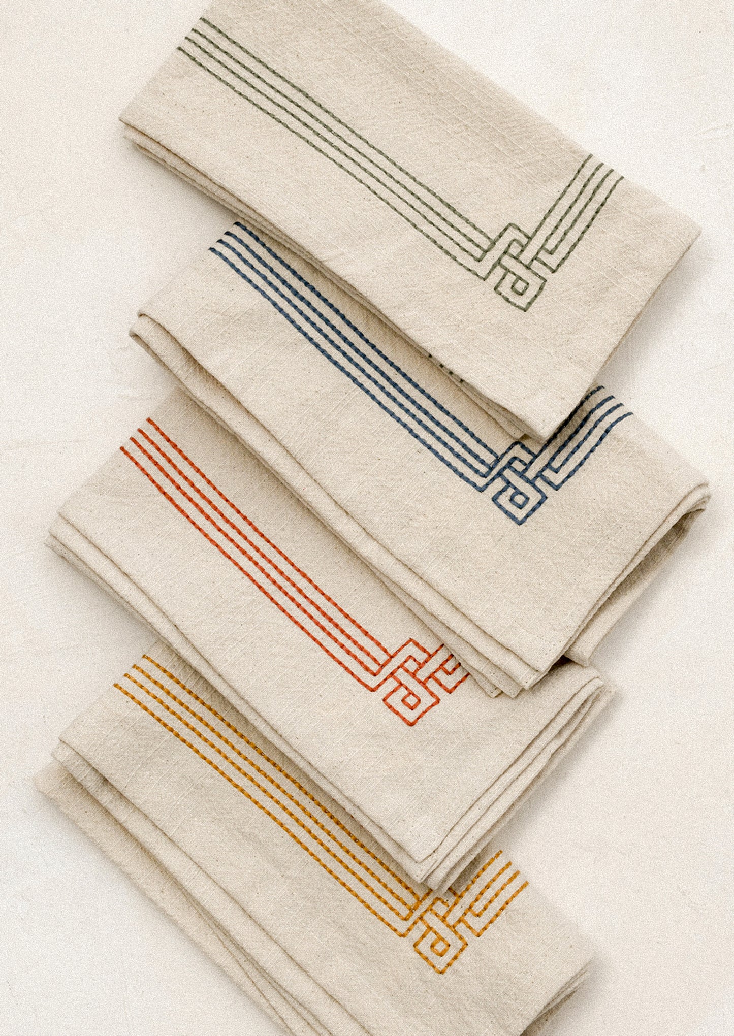 Set of beige napkins with embroidered geometric patterns in various colors on a white surface.