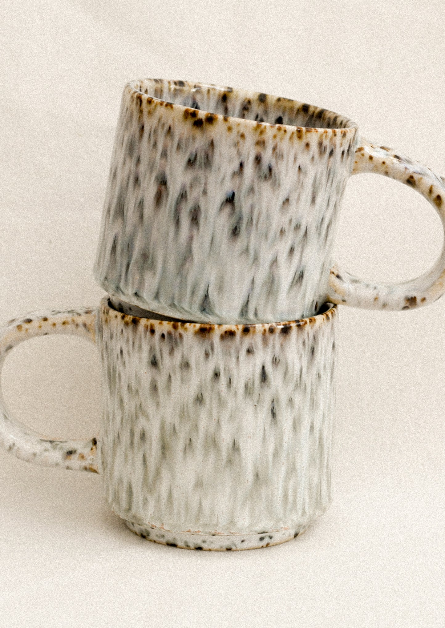 Two ceramic mugs with speckled pattern stacked on a light background