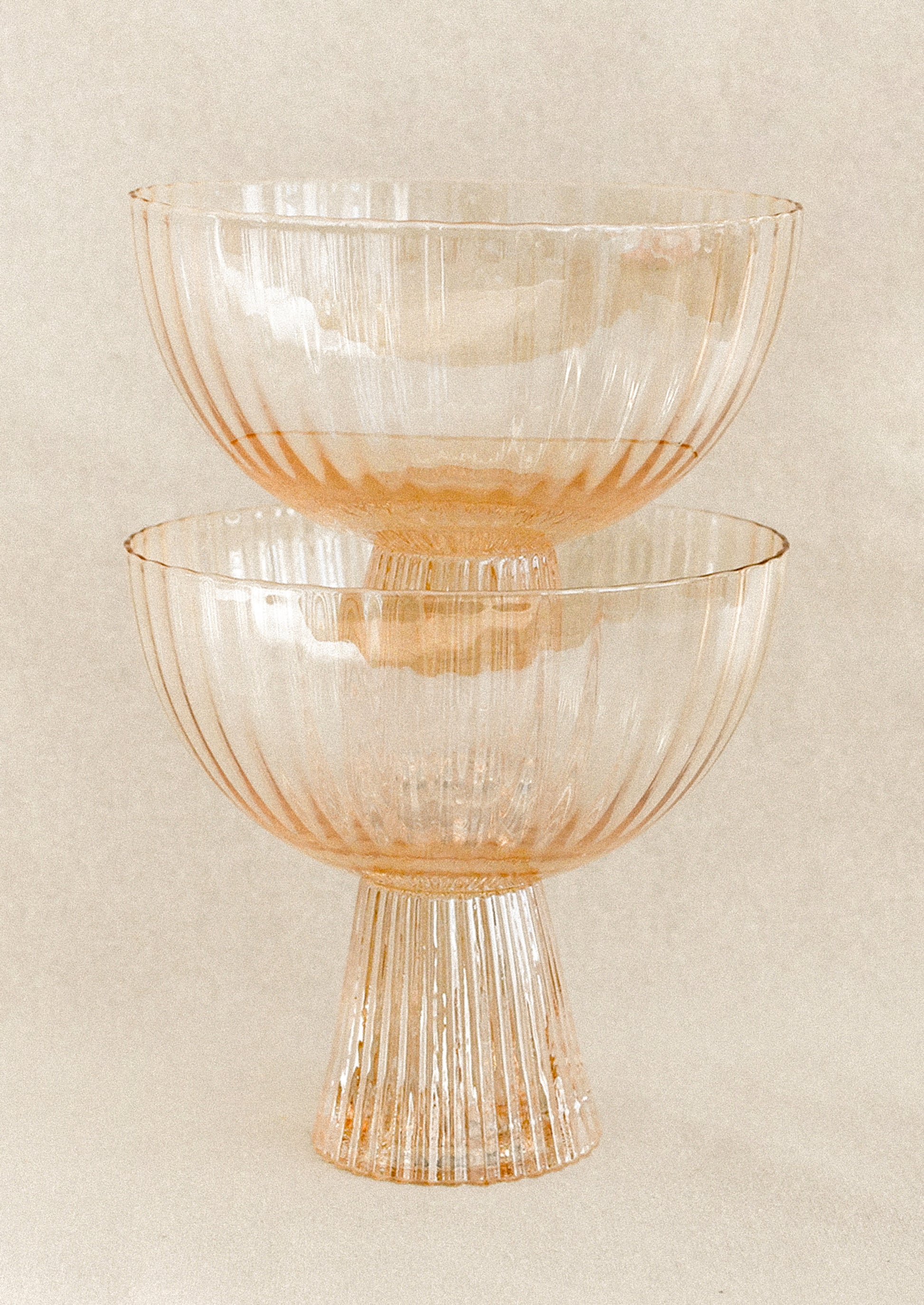 A coupe glass with fluted texture in peach color with iridescent finish.