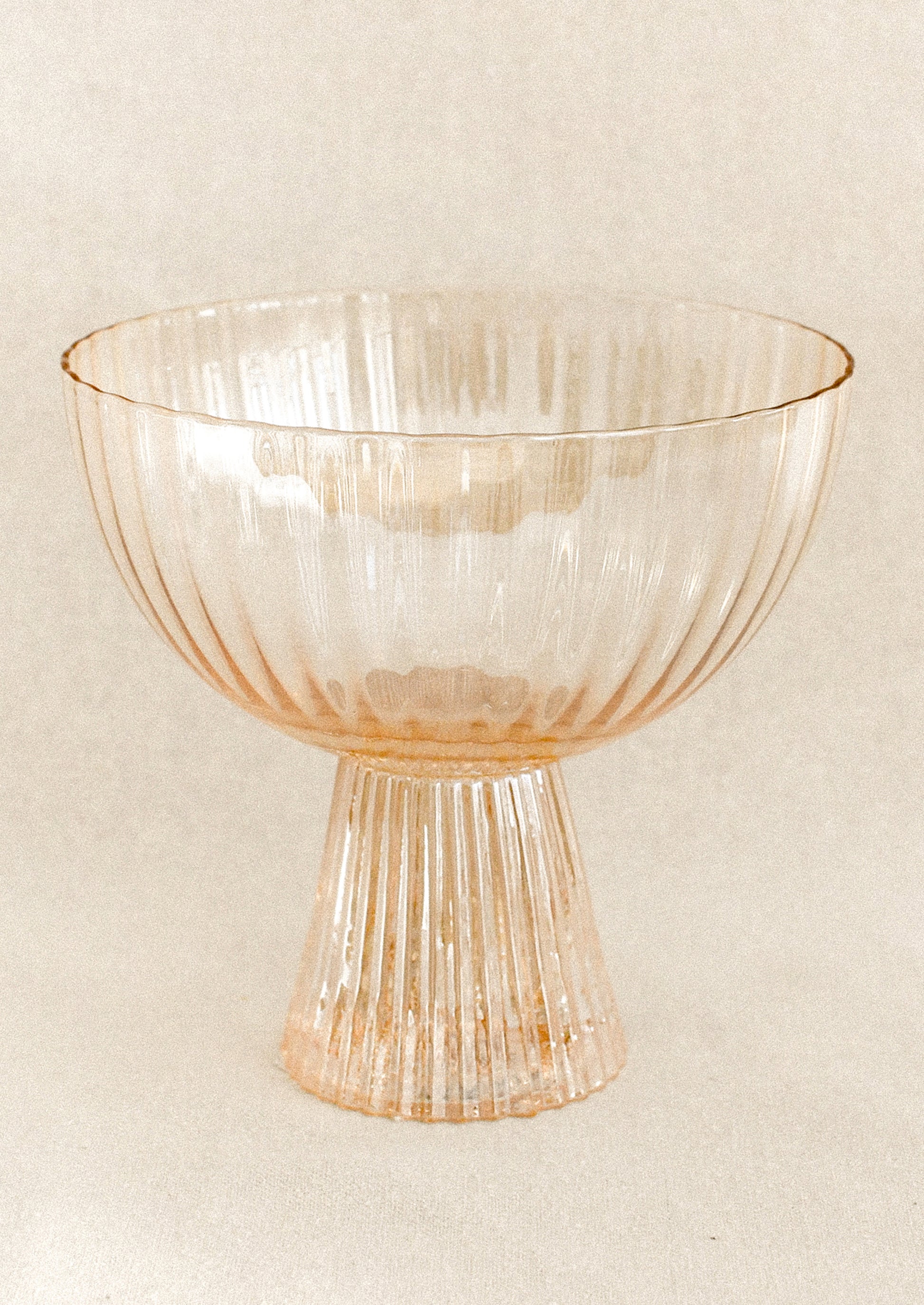 A coupe glass with fluted texture in peach color with iridescent finish.