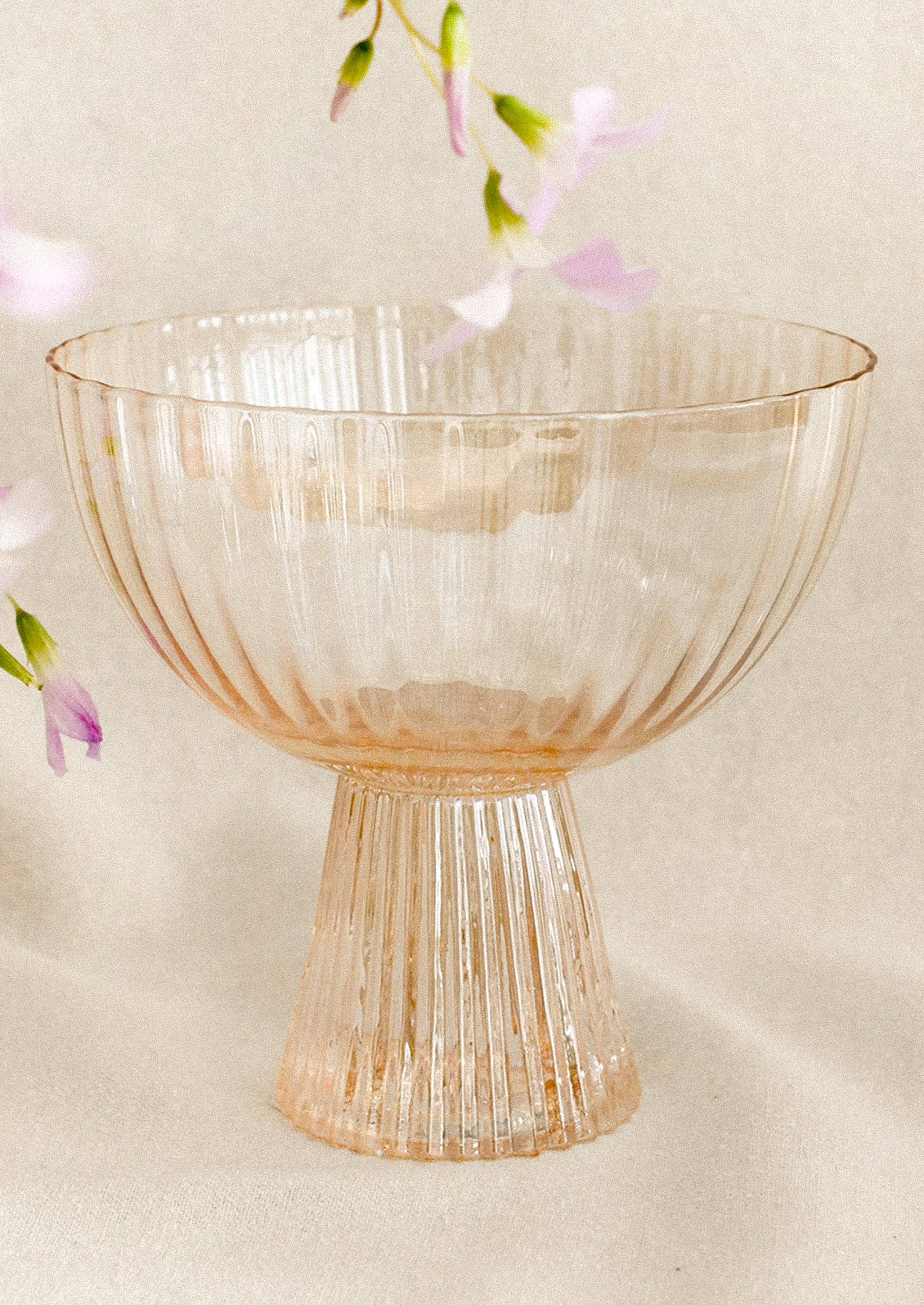 A coupe glass with fluted texture in peach color with iridescent finish.