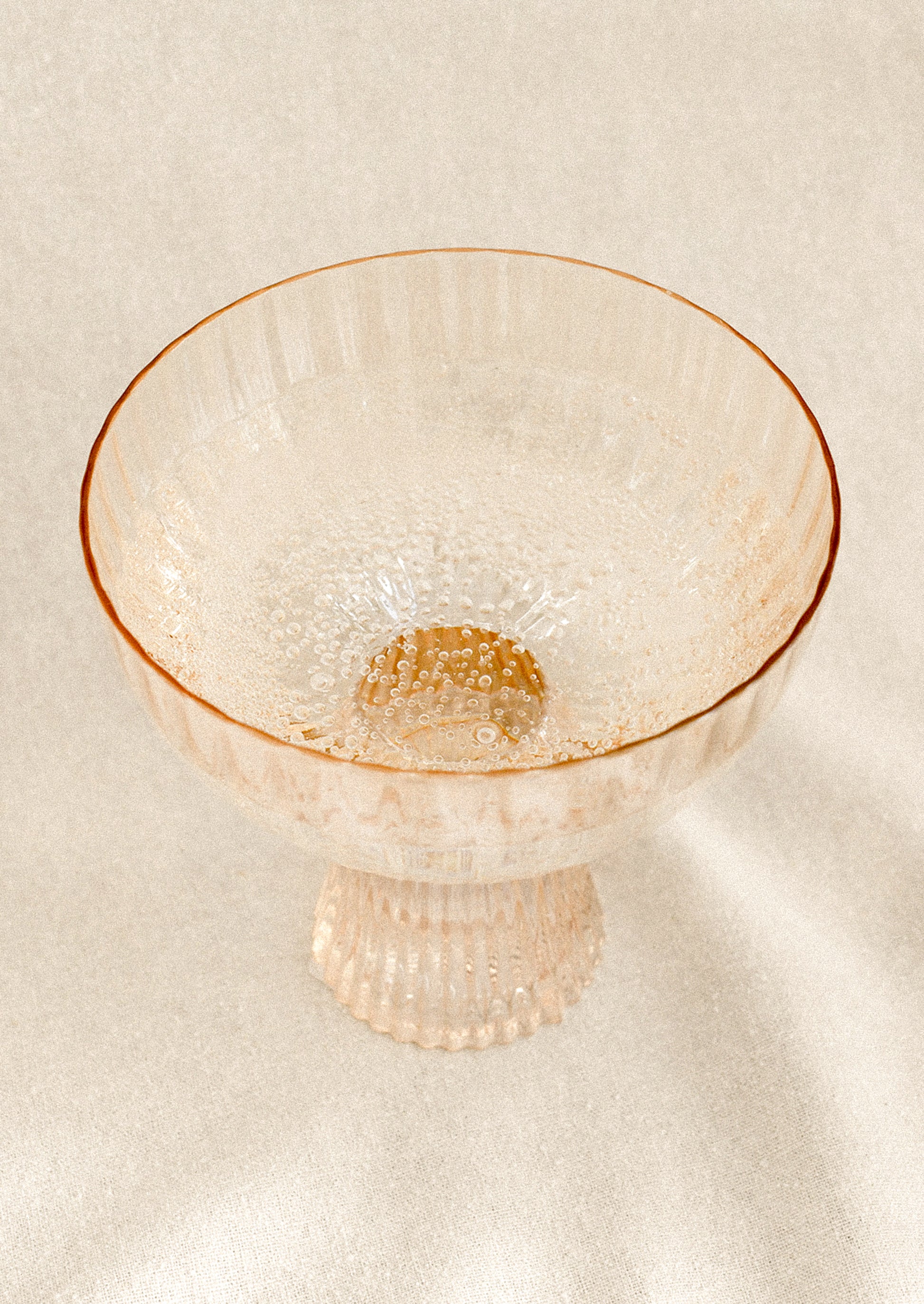 A coupe glass with fluted texture in peach color with iridescent finish.