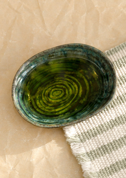 A small ceramic sauce dish in oval shape and deep emerald green reactive glaze.