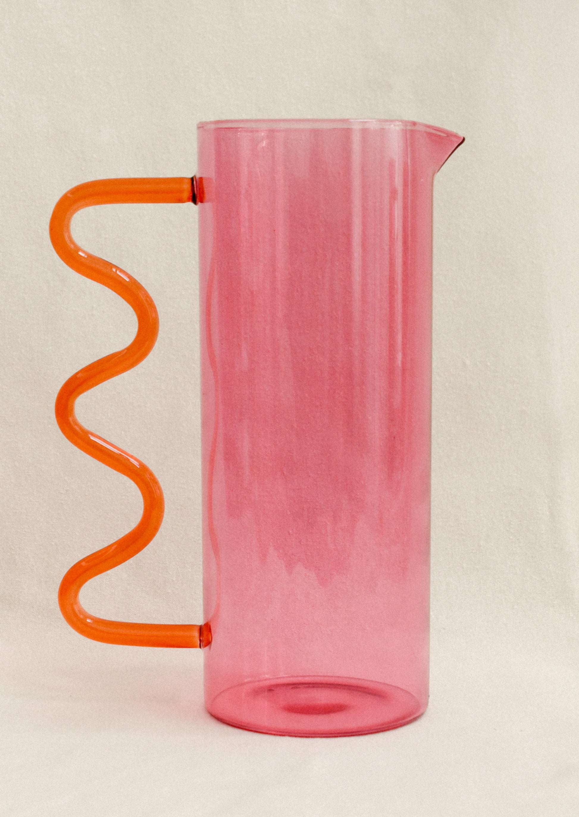 A pink glass pitcher with squiggle shaped handle in orange.