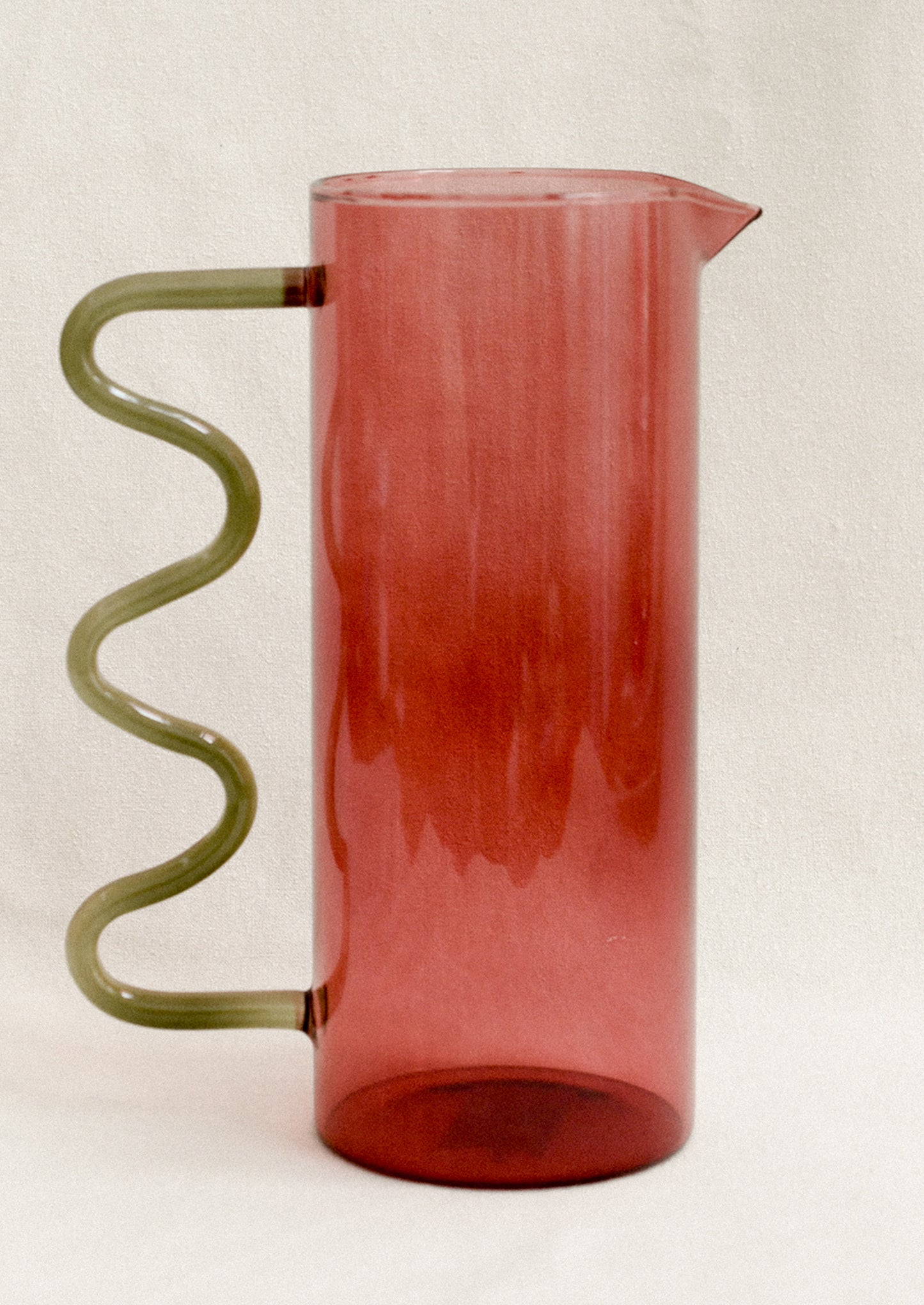 A two tone glass pitcher with squiggle shaped handle in smoky rose and sage green.