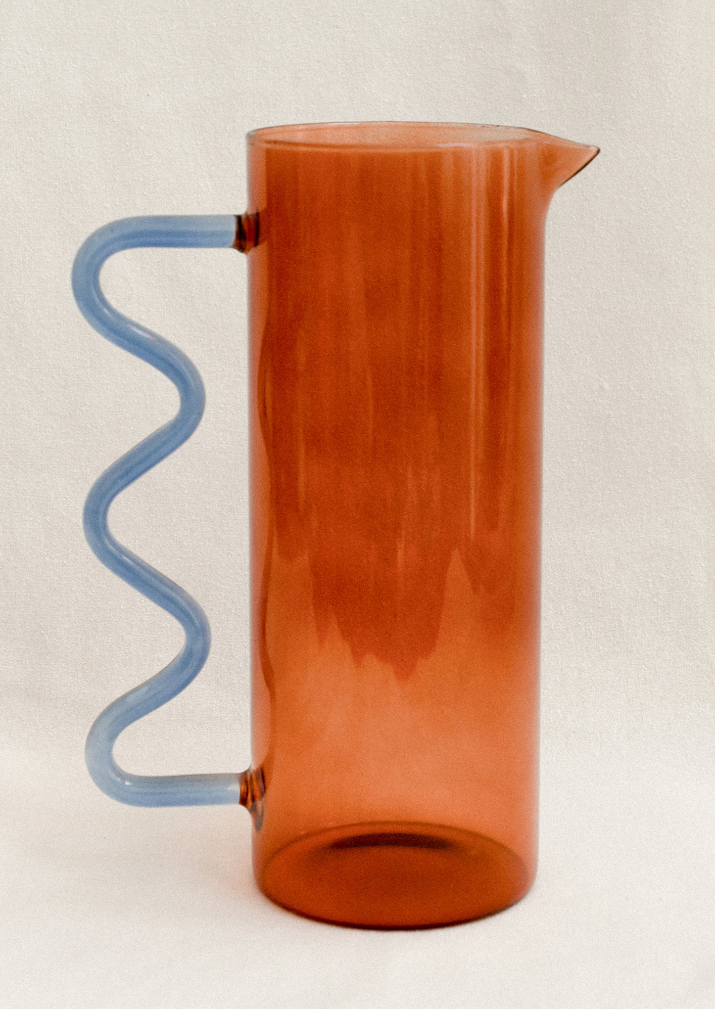 An amber glass pitcher with squiggle shaped handle in blue.
