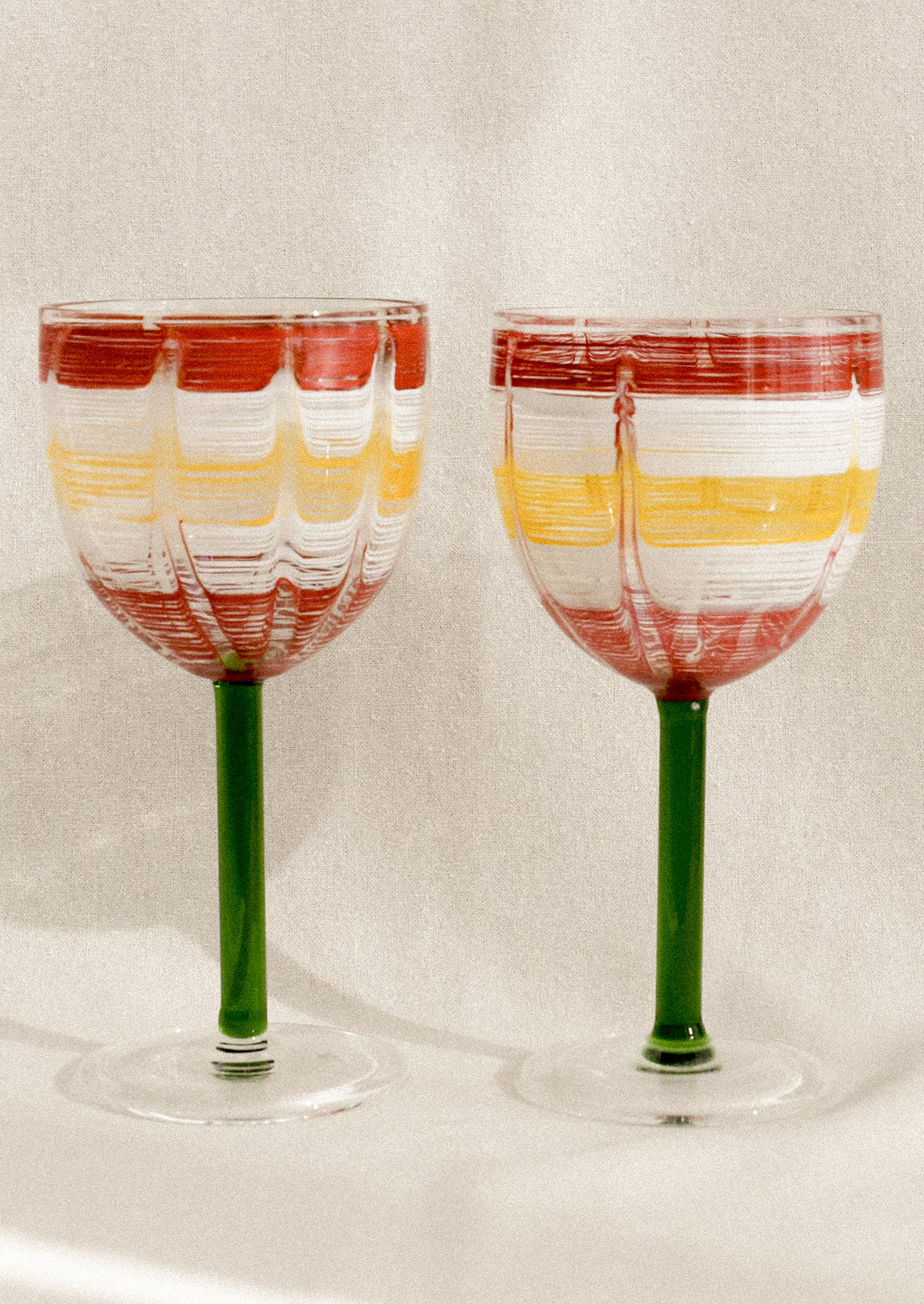 A wine glass with green stem and hand painted cup with abstract line pattern.
