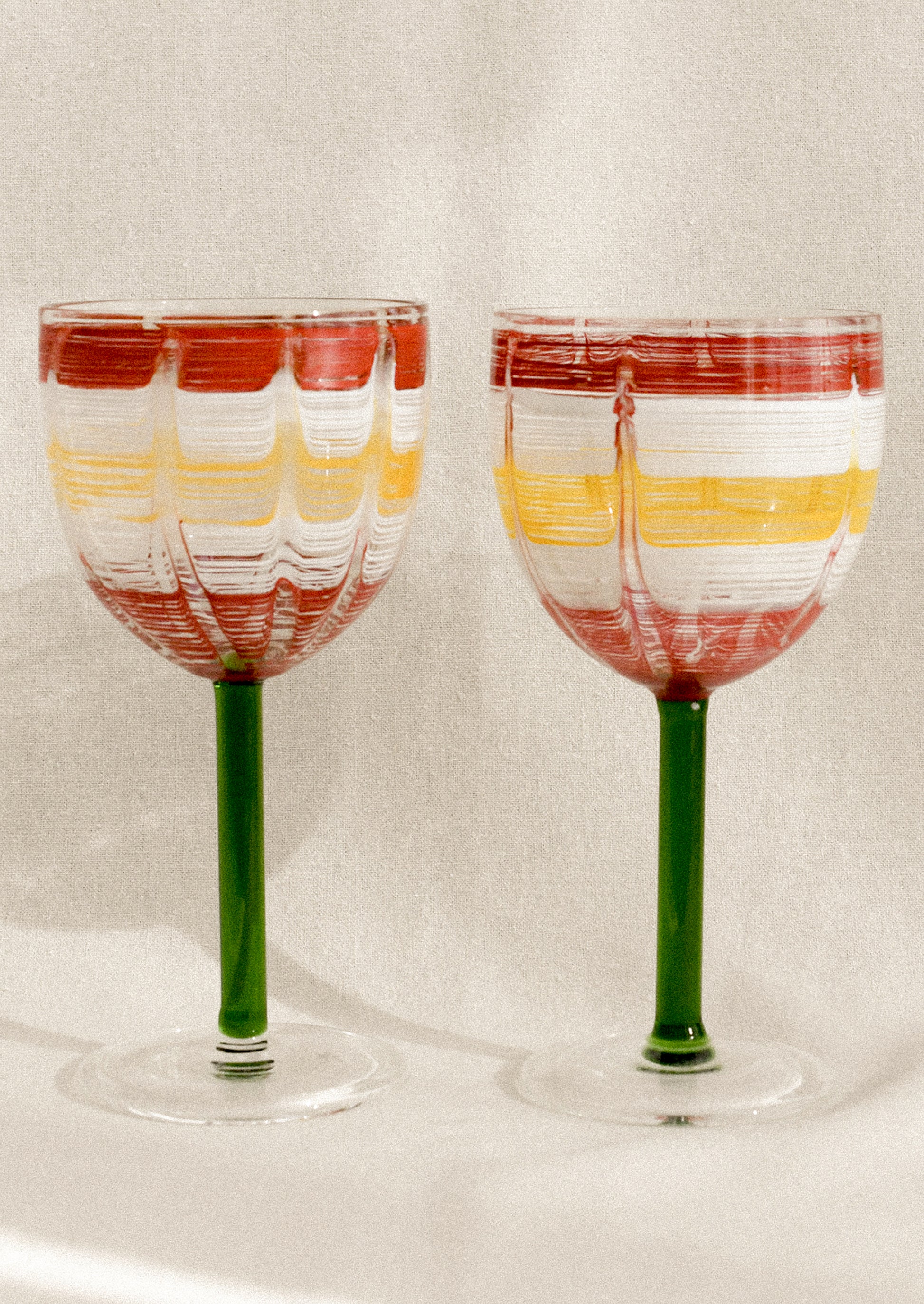 A wine glass with green stem and hand painted cup with abstract line pattern.