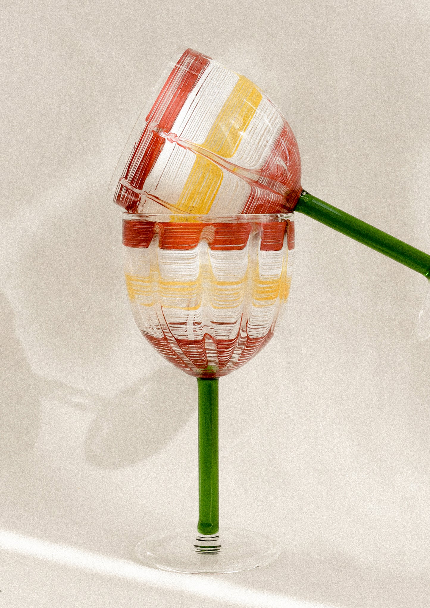 A wine glass with green stem and hand painted cup with abstract line pattern.