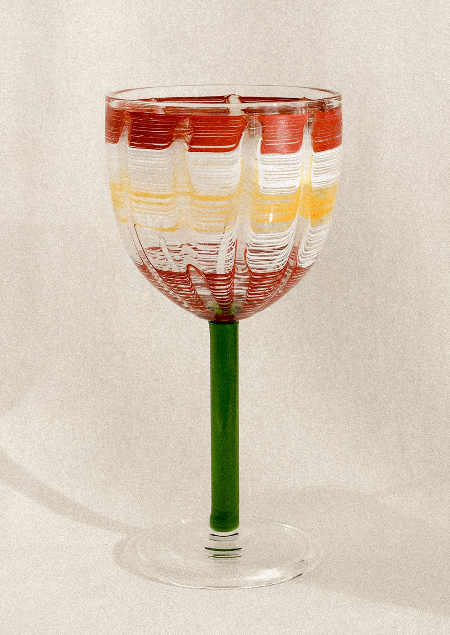A wine glass with green stem and hand painted cup with abstract line pattern.