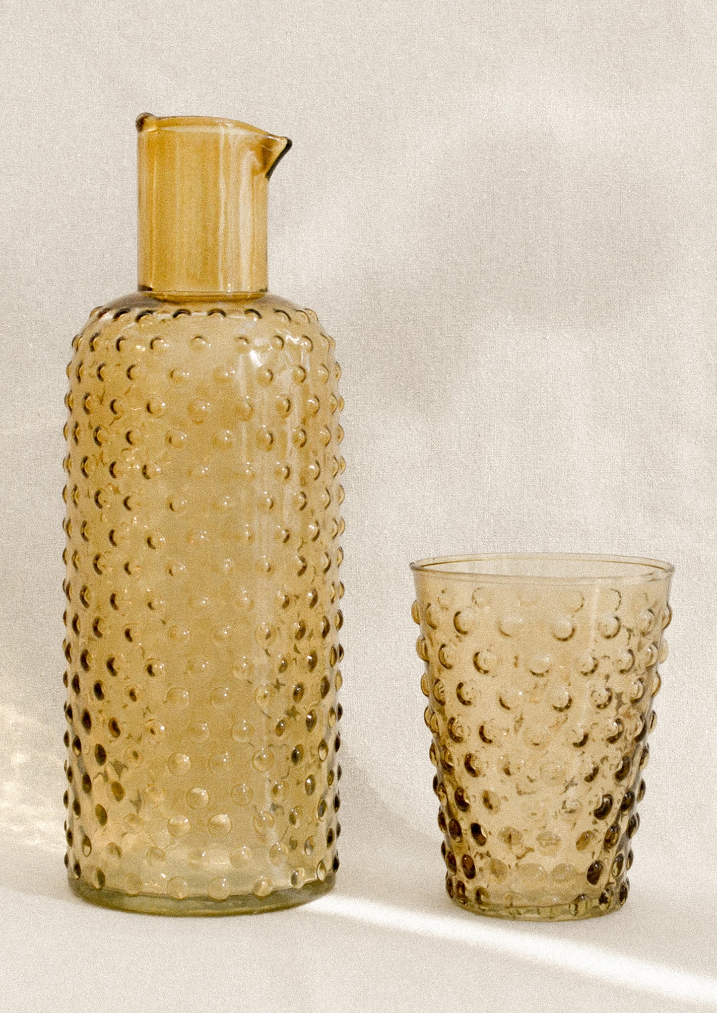 A carafe and cup set with hobnail texture in amber color.