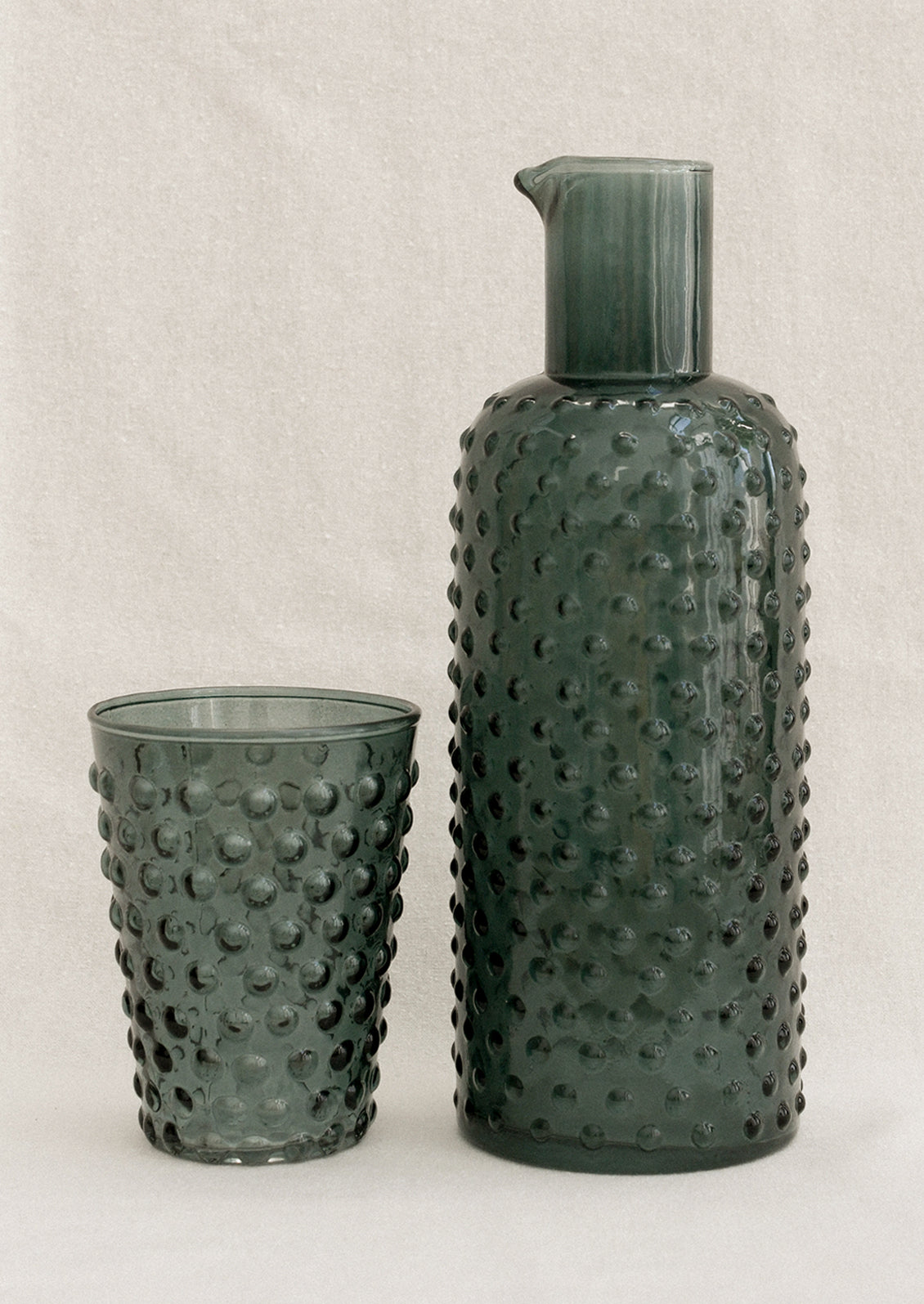 A carafe and cup set with hobnail texture in petrol color.
