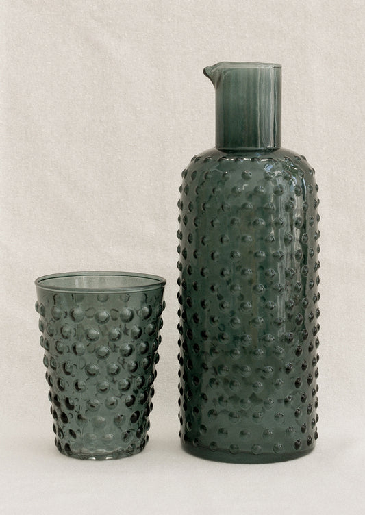 A carafe and cup set with hobnail texture in petrol color.