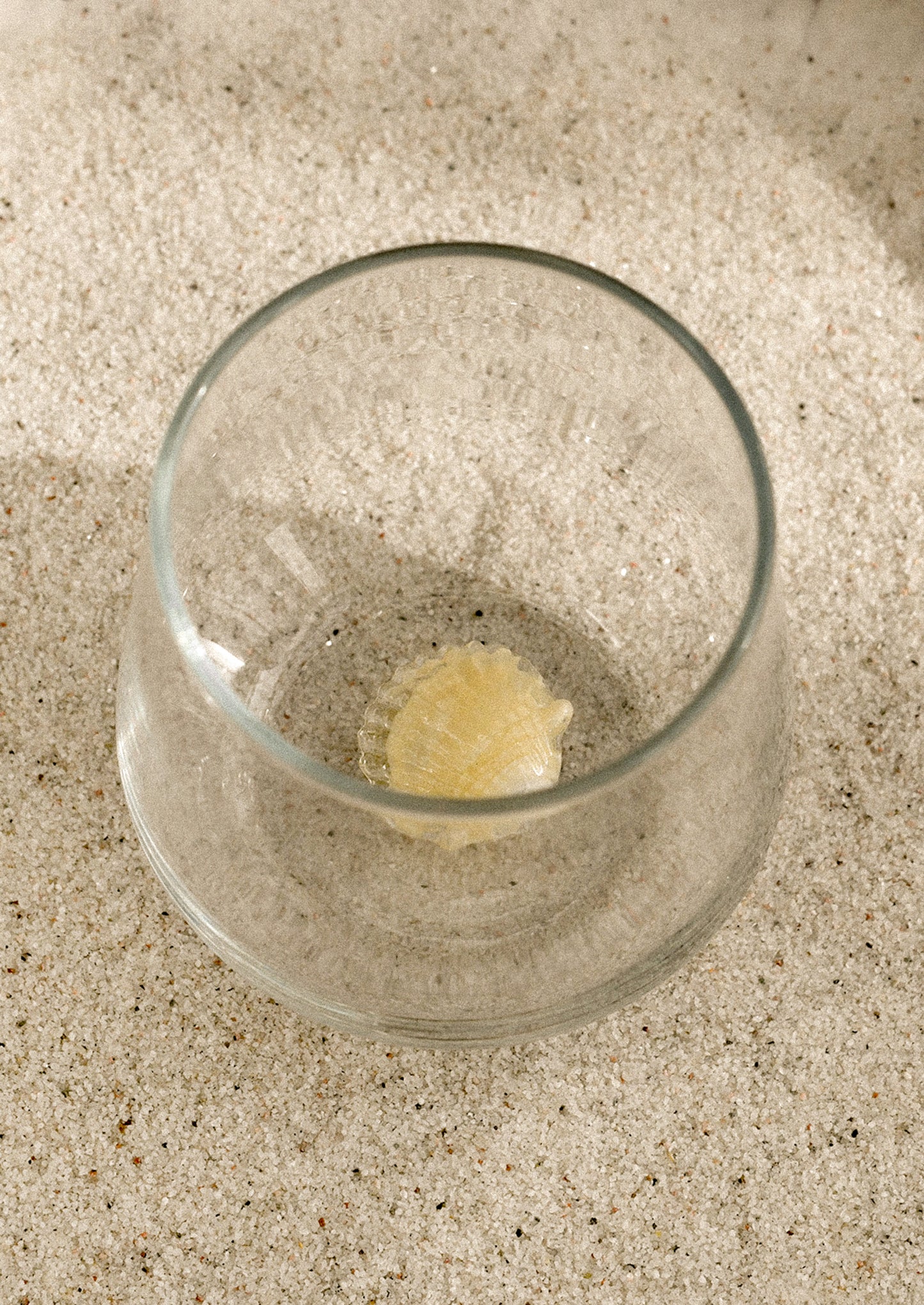 A clear stemless glass with three-dimensional shell detail at bottom of glass.